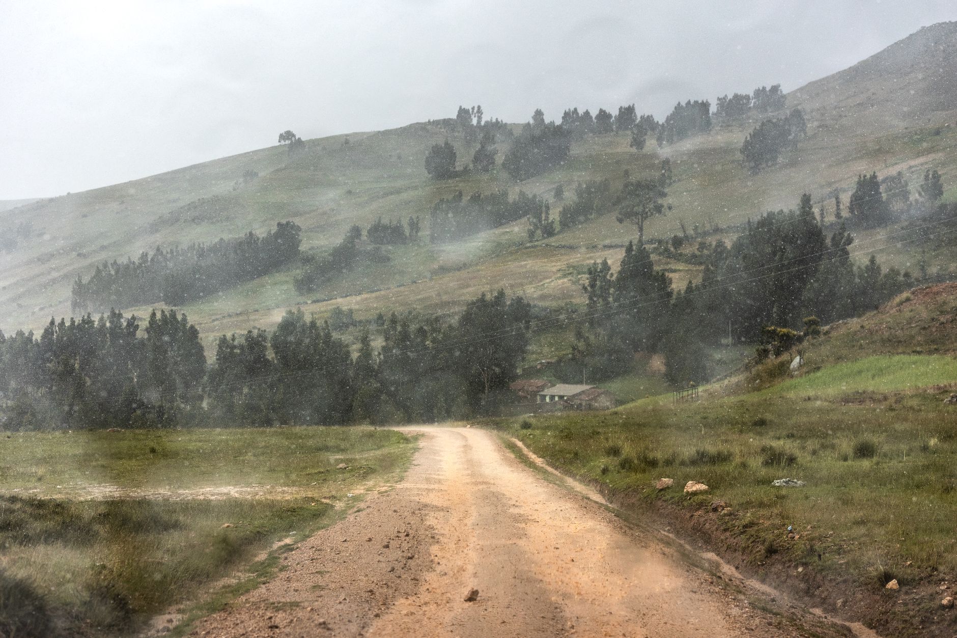 Dirt road cutting through a rainy mountainous landscape in rural Peru.