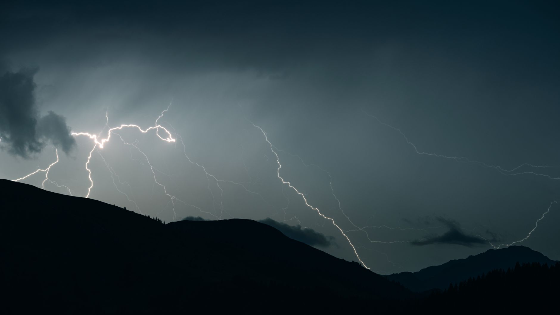 Captivating shot of lightning illuminating a dark sky over mountain silhouettes during a thunderstorm.