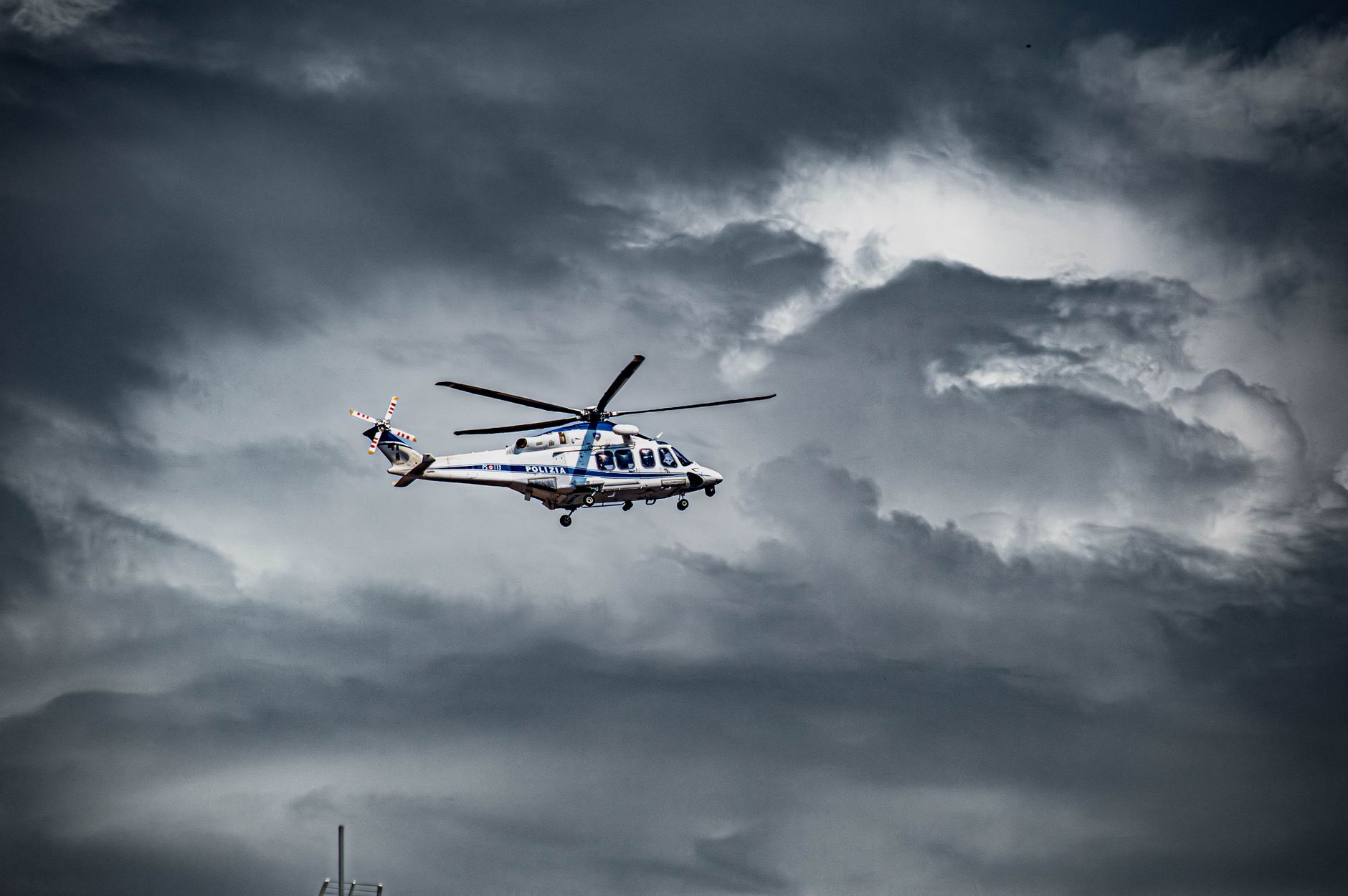 A helicopter soars beneath dark and dramatic storm clouds, capturing a sense of adventure and urgency.