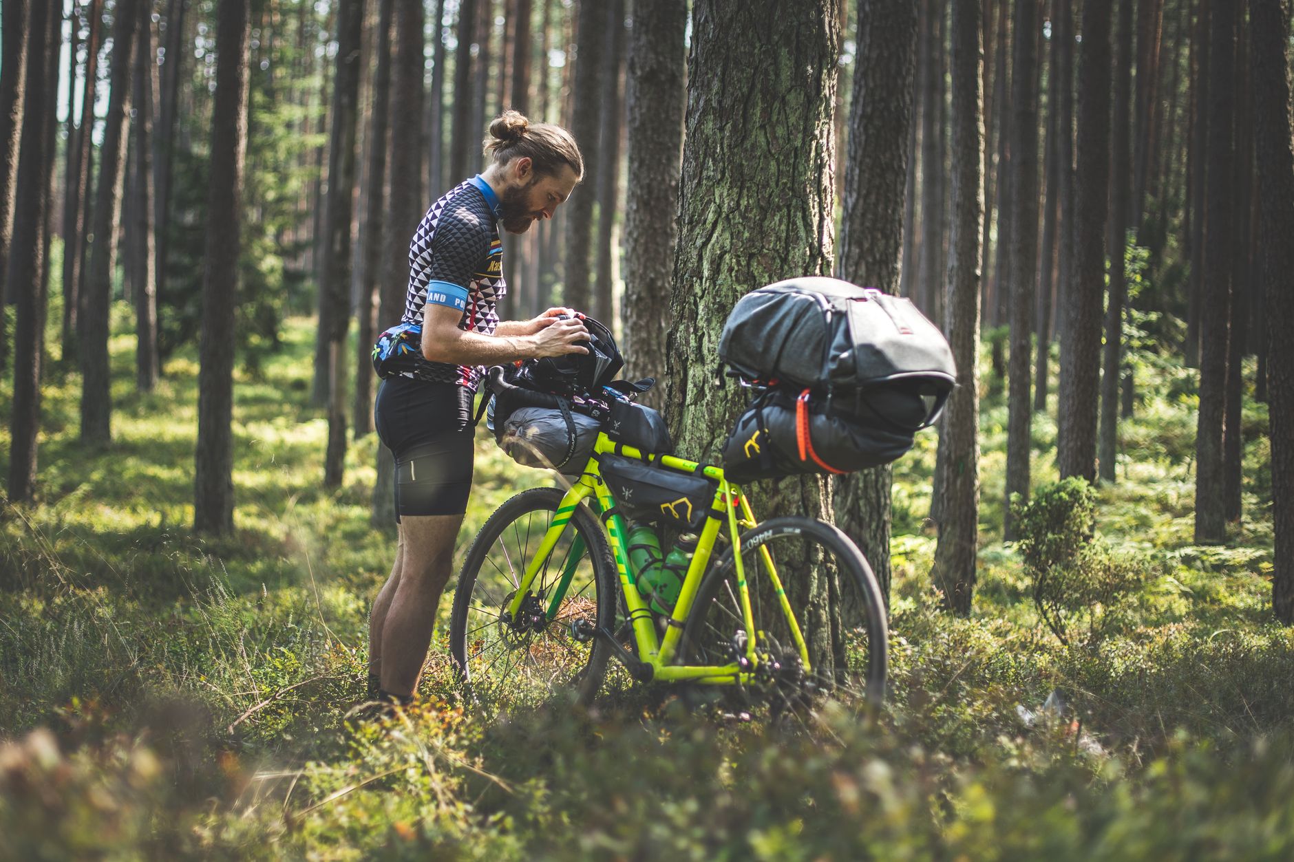 Cyclist checking gear during bikepacking trip in a lush Polish forest.