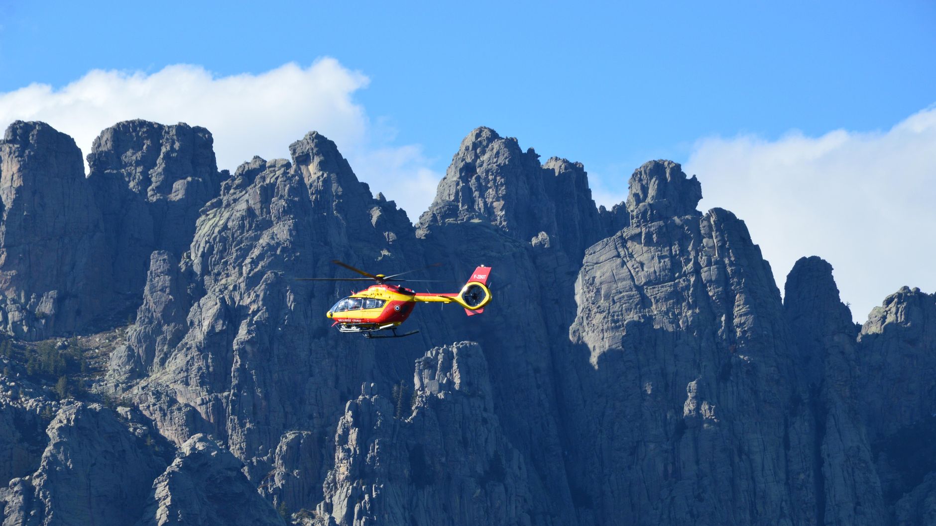 A red and yellow rescue helicopter in flight over the rugged Zonza mountains in Corse, France.