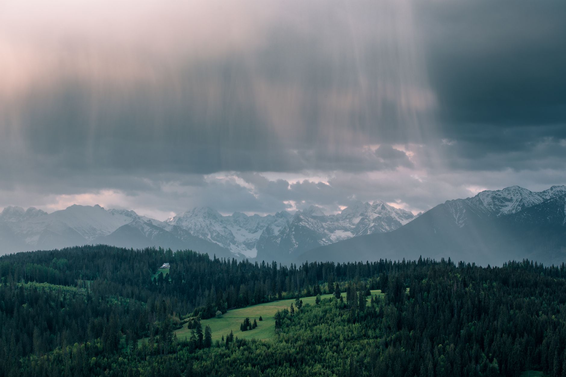 View of the Tatra Mountains during a rainy day with dramatic clouds and lush green forests.
