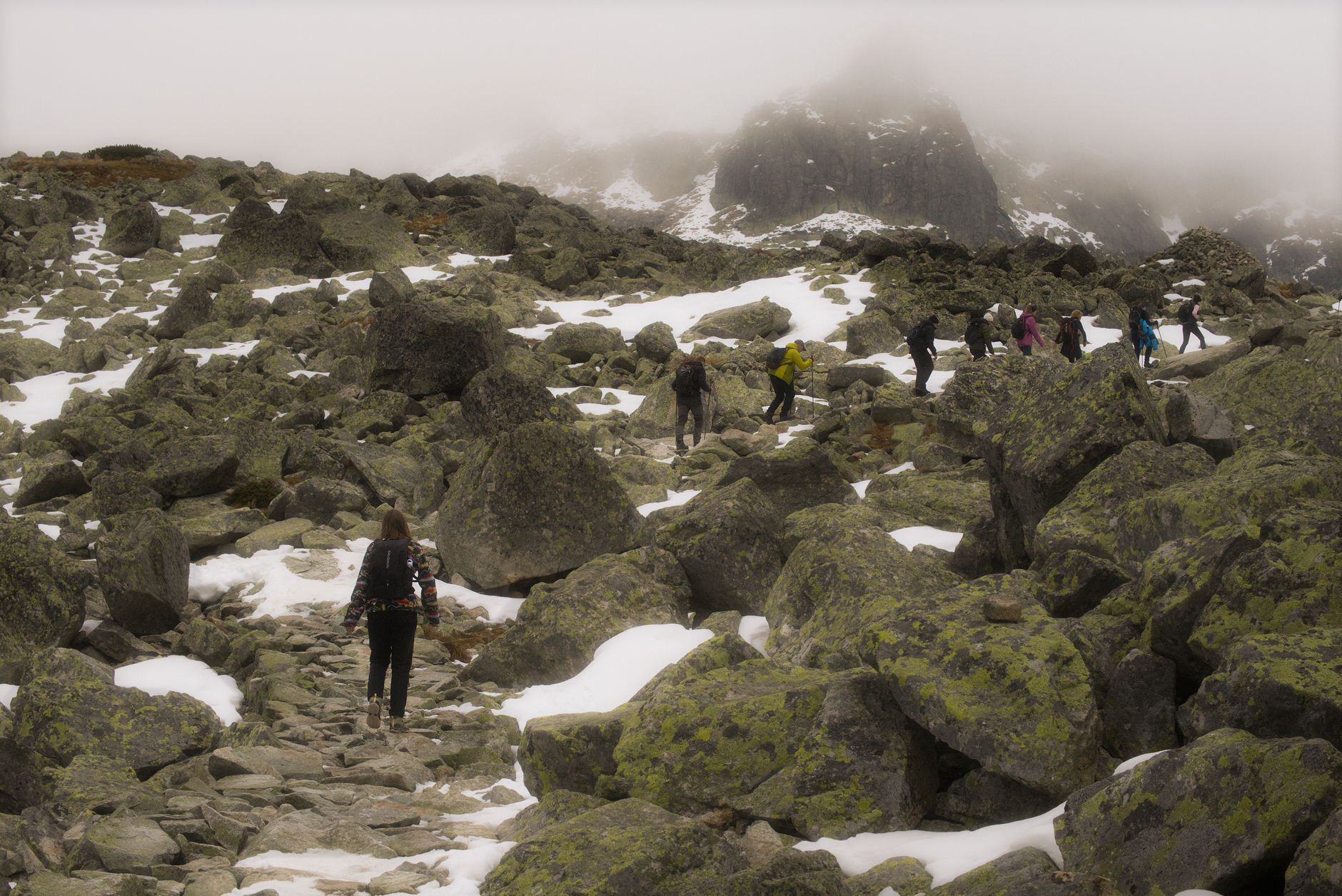Adventurers hike rocky terrain in Slovakia's Tatra Mountains under cloudy skies.