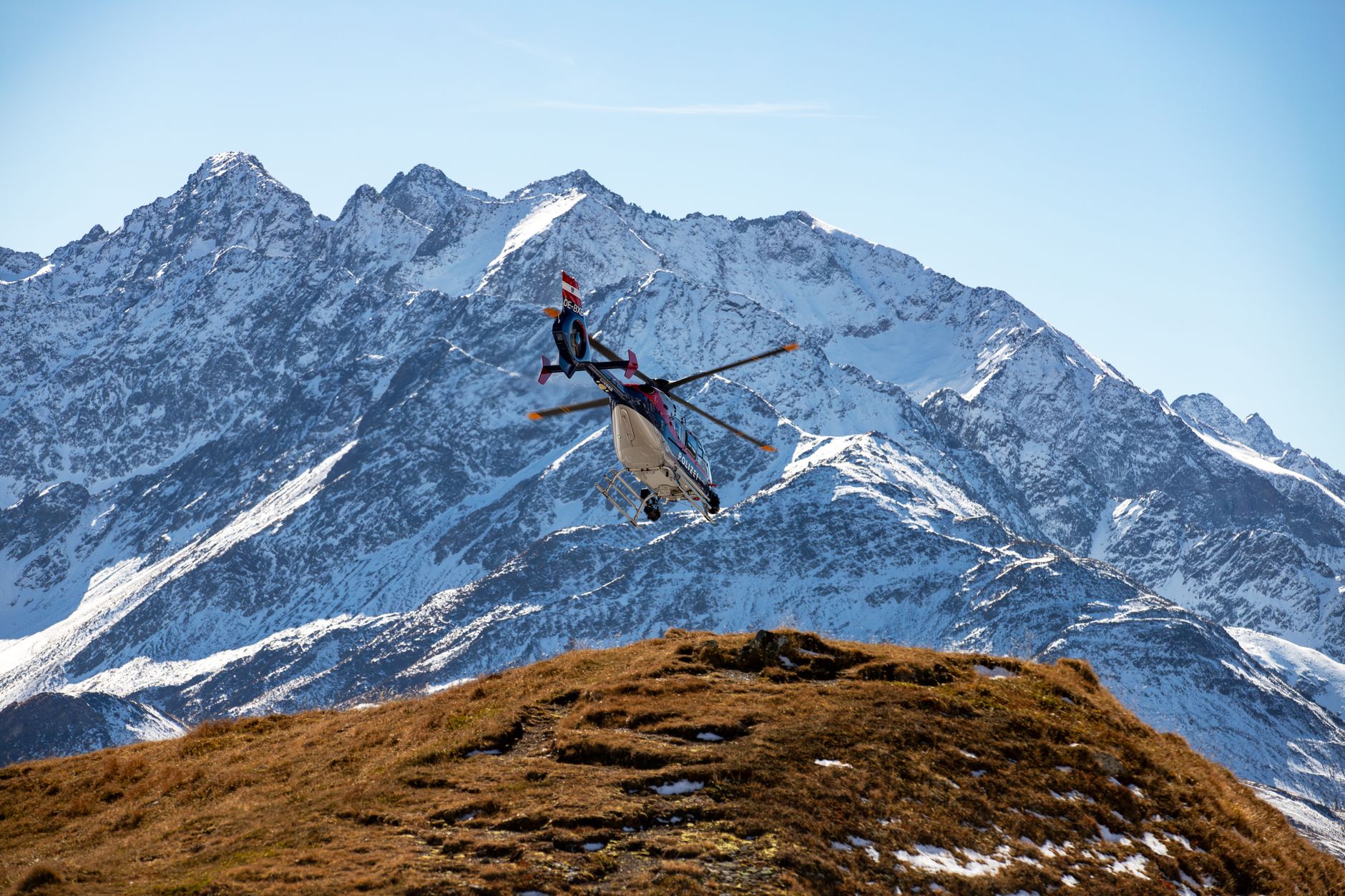 A helicopter flies over the snowy peaks of the Korutany mountains on a clear day.
