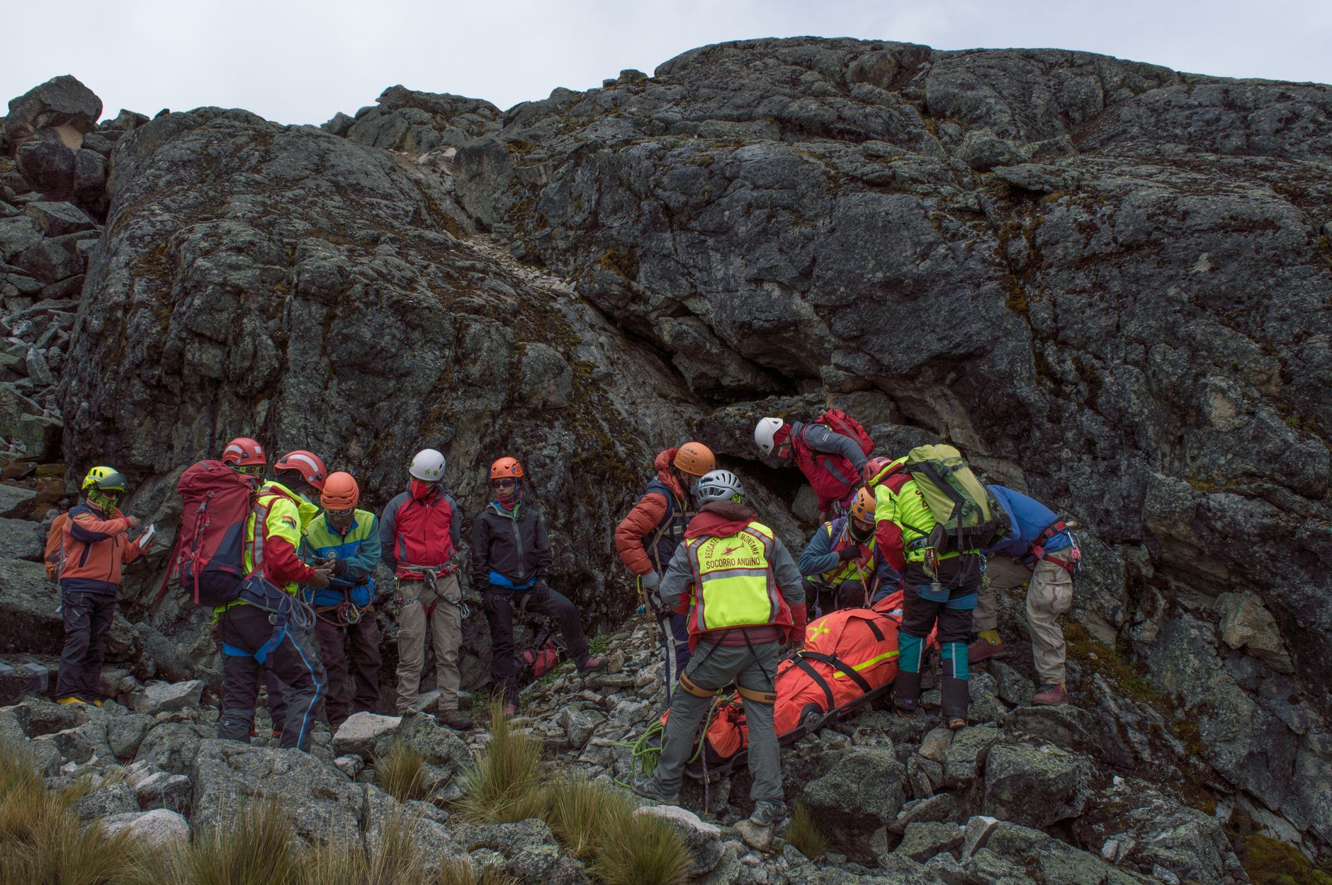 A rescue team aids an injured hiker on a rocky mountain slope during daylight.