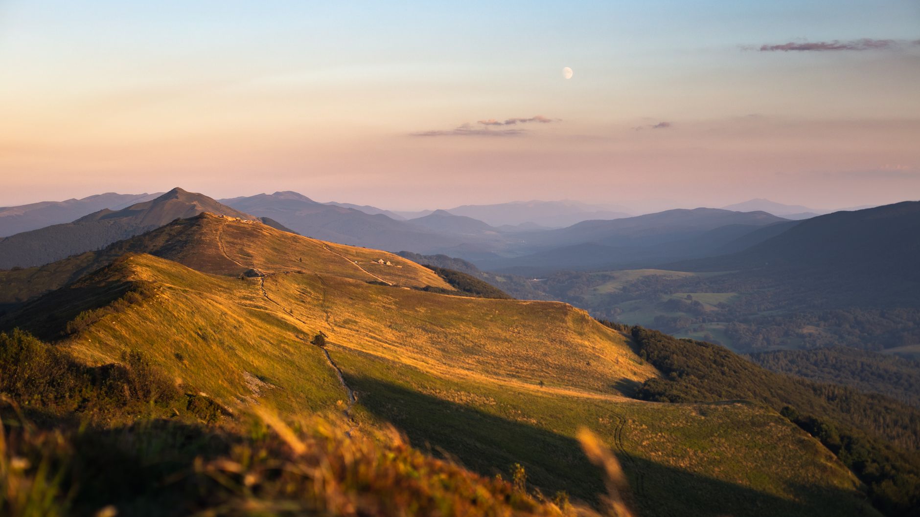 Peaceful sunset over the Bieszczady Mountains, showcasing sweeping hills and valleys under soft pastel skies.