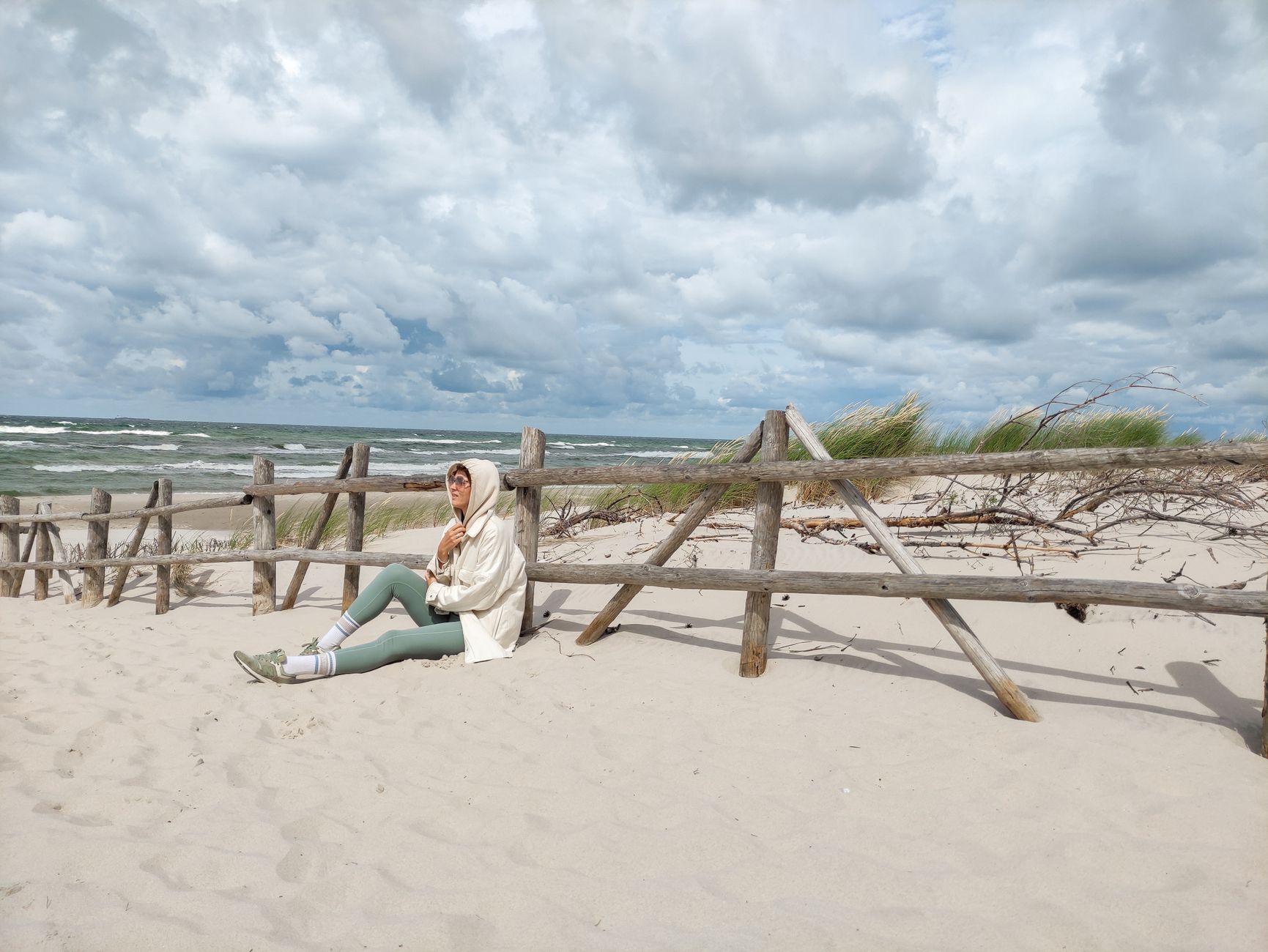 Person in casual attire sits on Baltic beach, enjoying the serene sea view.