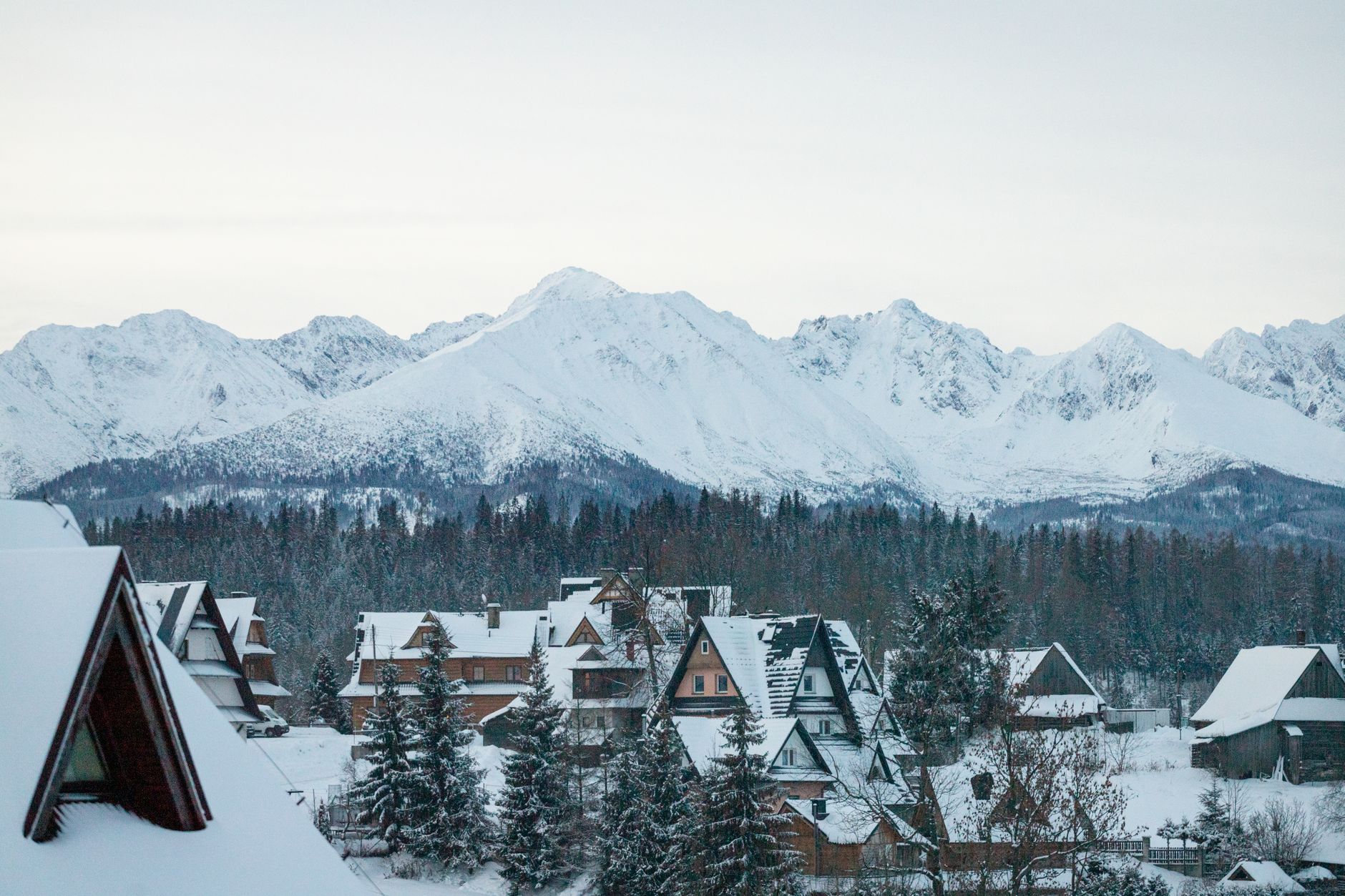 Charming winter scene in a Polish village with snowy rooftops and mountain backdrop.