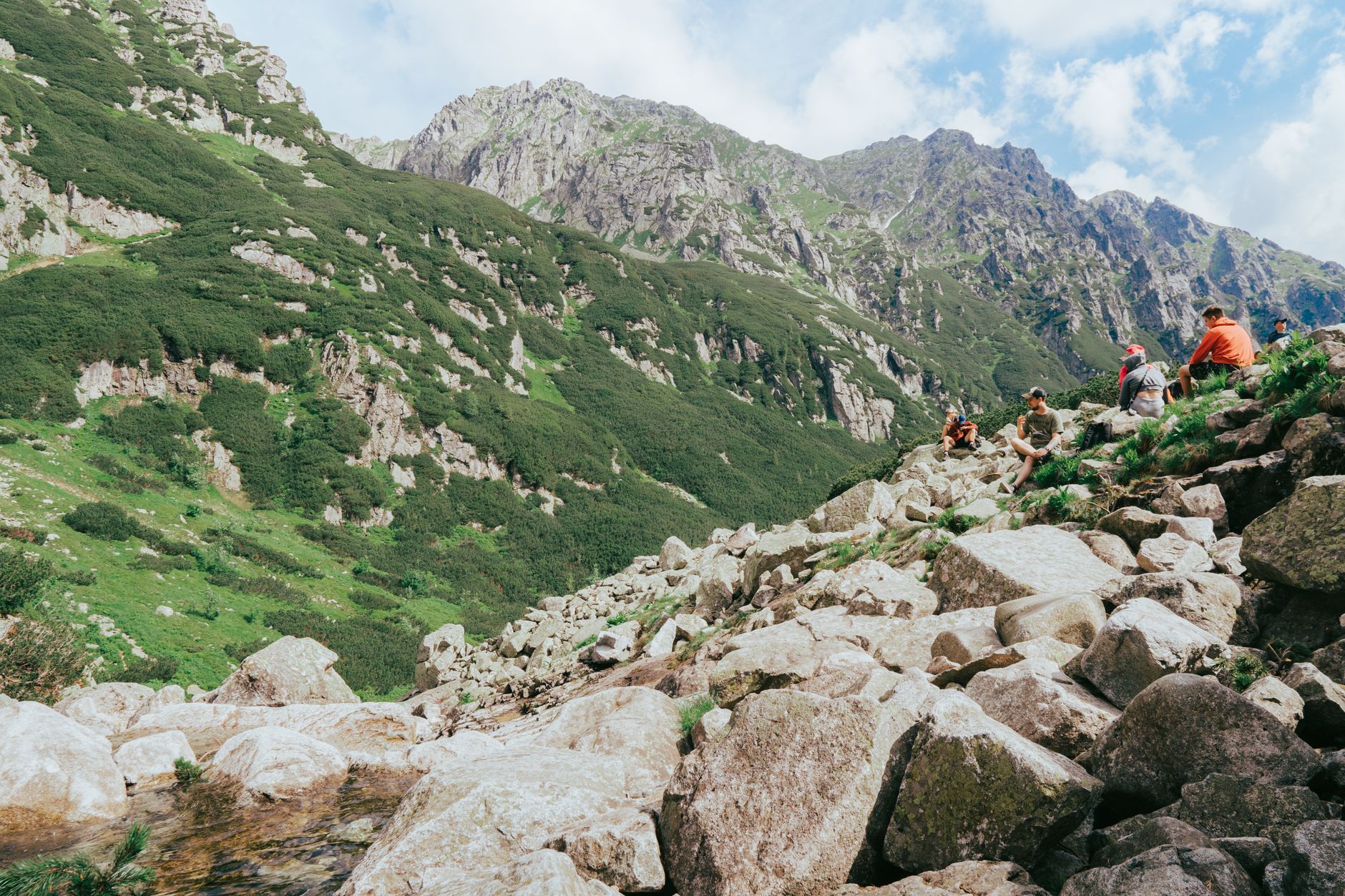 A group of hikers resting on a rocky slope in the picturesque Tatra Mountains under a clear summer sky.