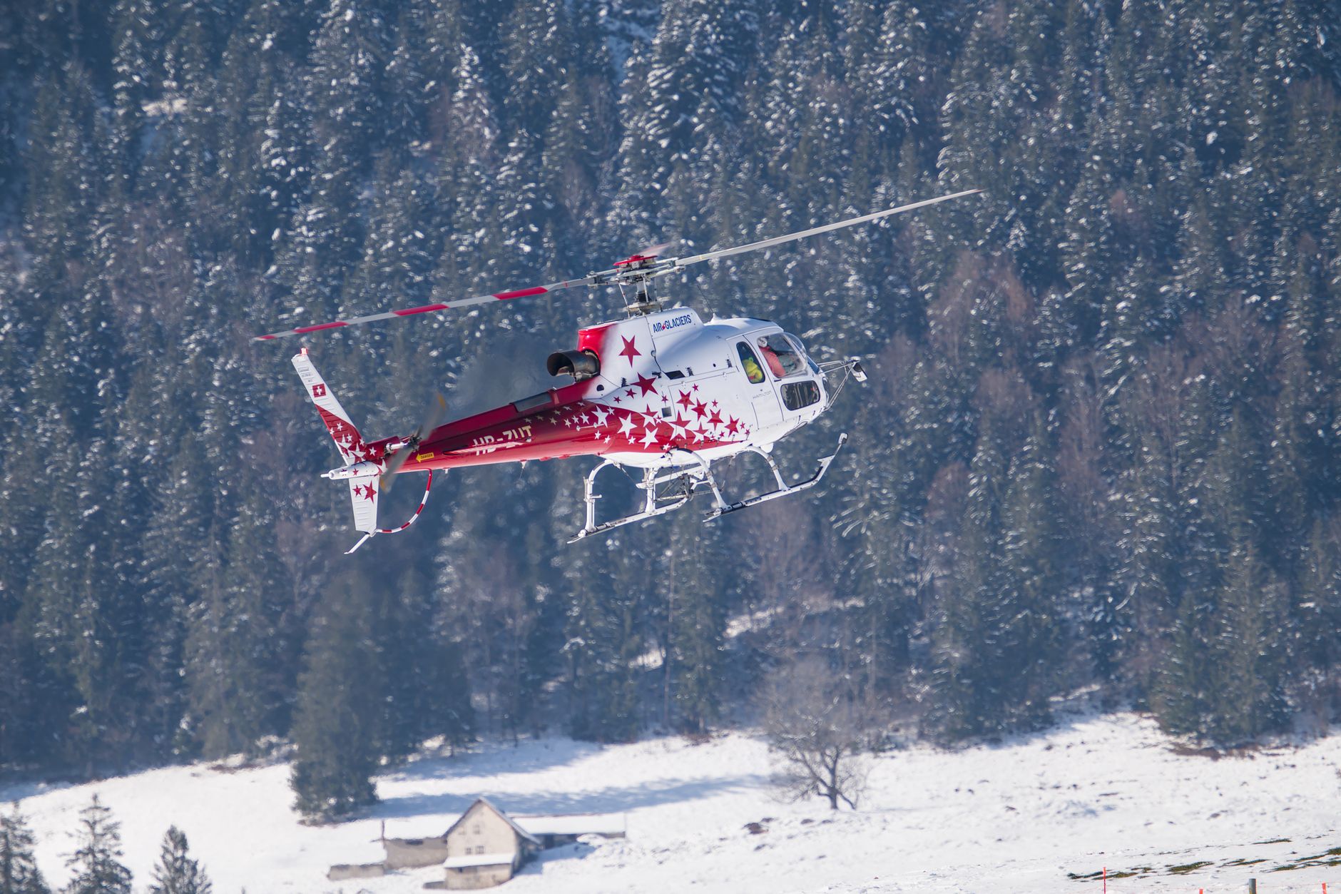 A helicopter adorned with red stars flying over snowy terrain in Switzerland.