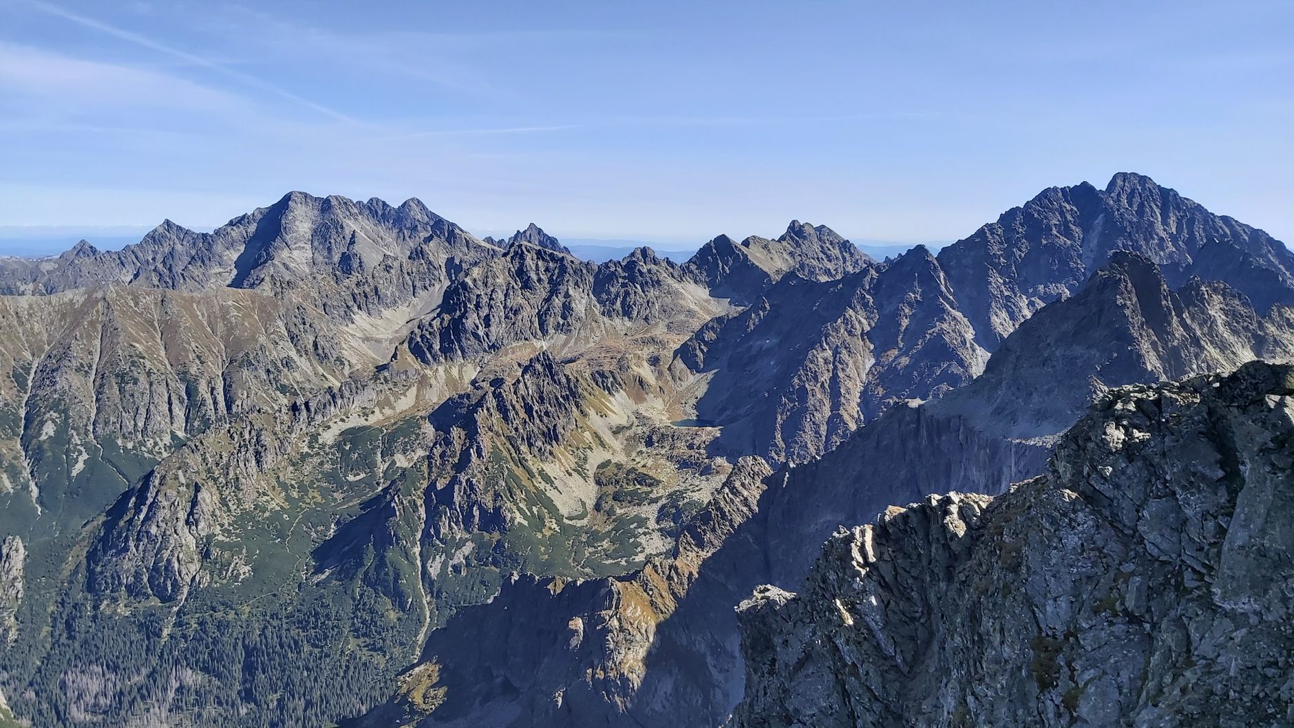 Panoramic view of the Tatra Mountains under a clear blue sky, showcasing rugged peaks and rocky cliffs.