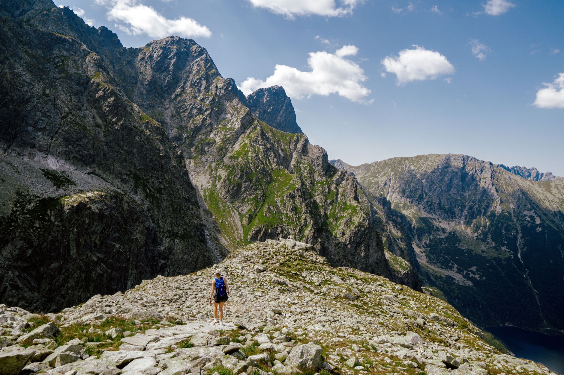 A hiker traverses the rugged terrain of the Tatra Mountains under a bright blue sky near Zakopane, Poland.