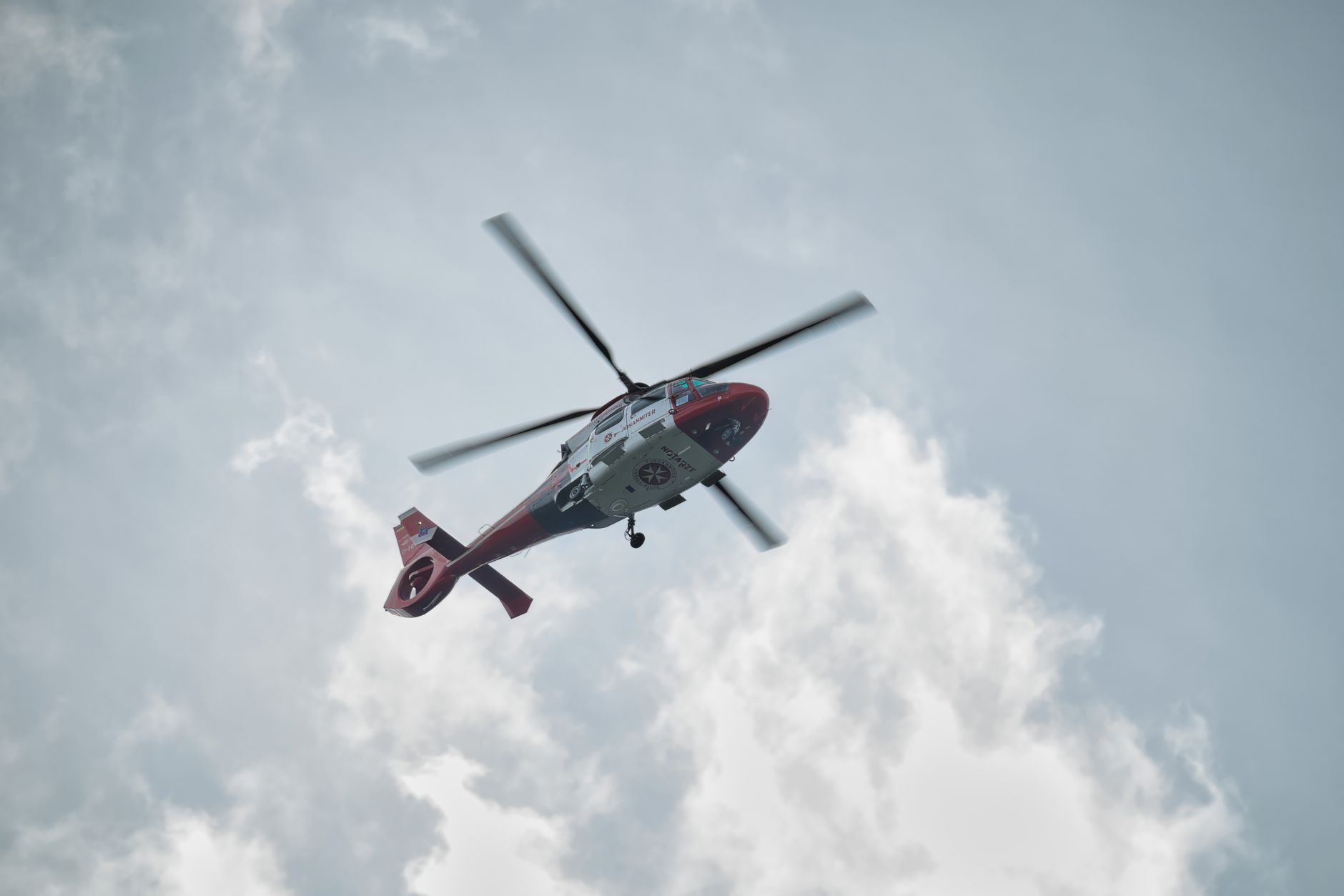A red and white rescue helicopter flying through a partly cloudy sky.