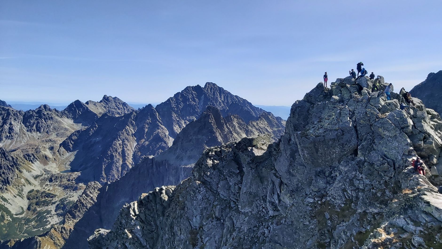 Adventurous hikers exploring the rugged peaks of the Tatra Mountains under clear skies.