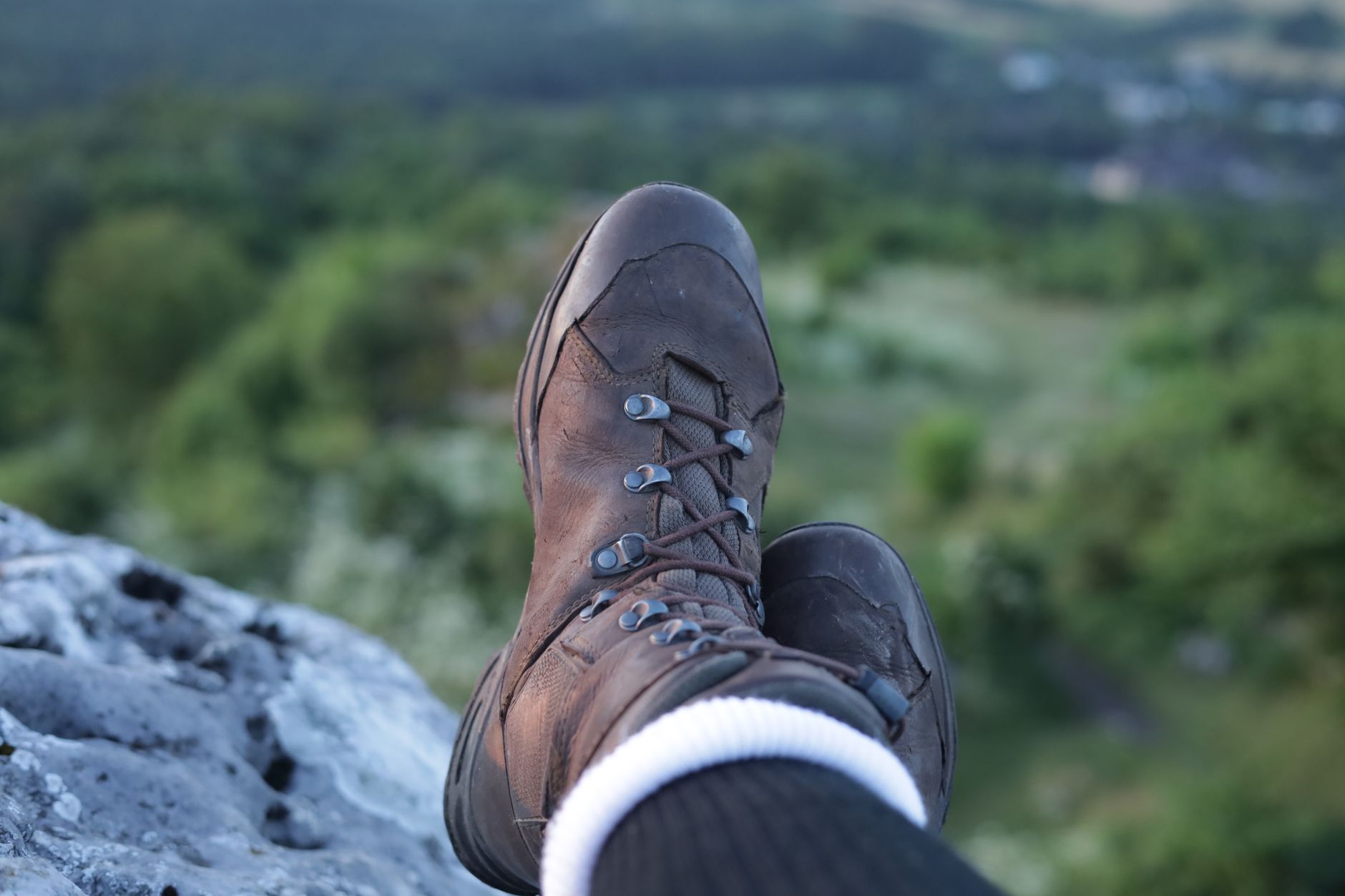 A pair of hiking boots resting on a cliff edge, overlooking a lush valley in Zborów, Poland.