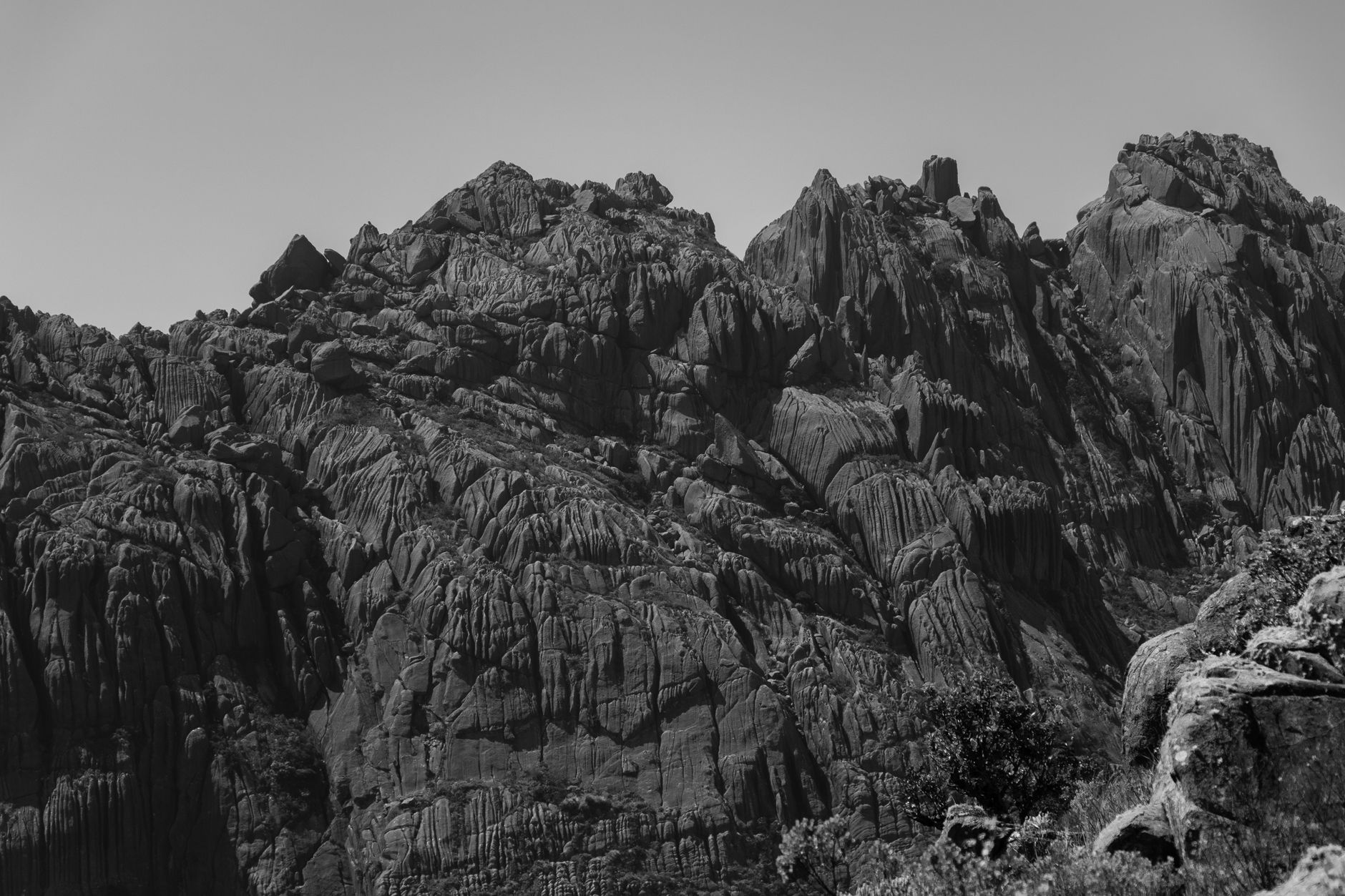 A dramatic black and white view of rugged mountain peaks with intricate rock formations under a clear sky.