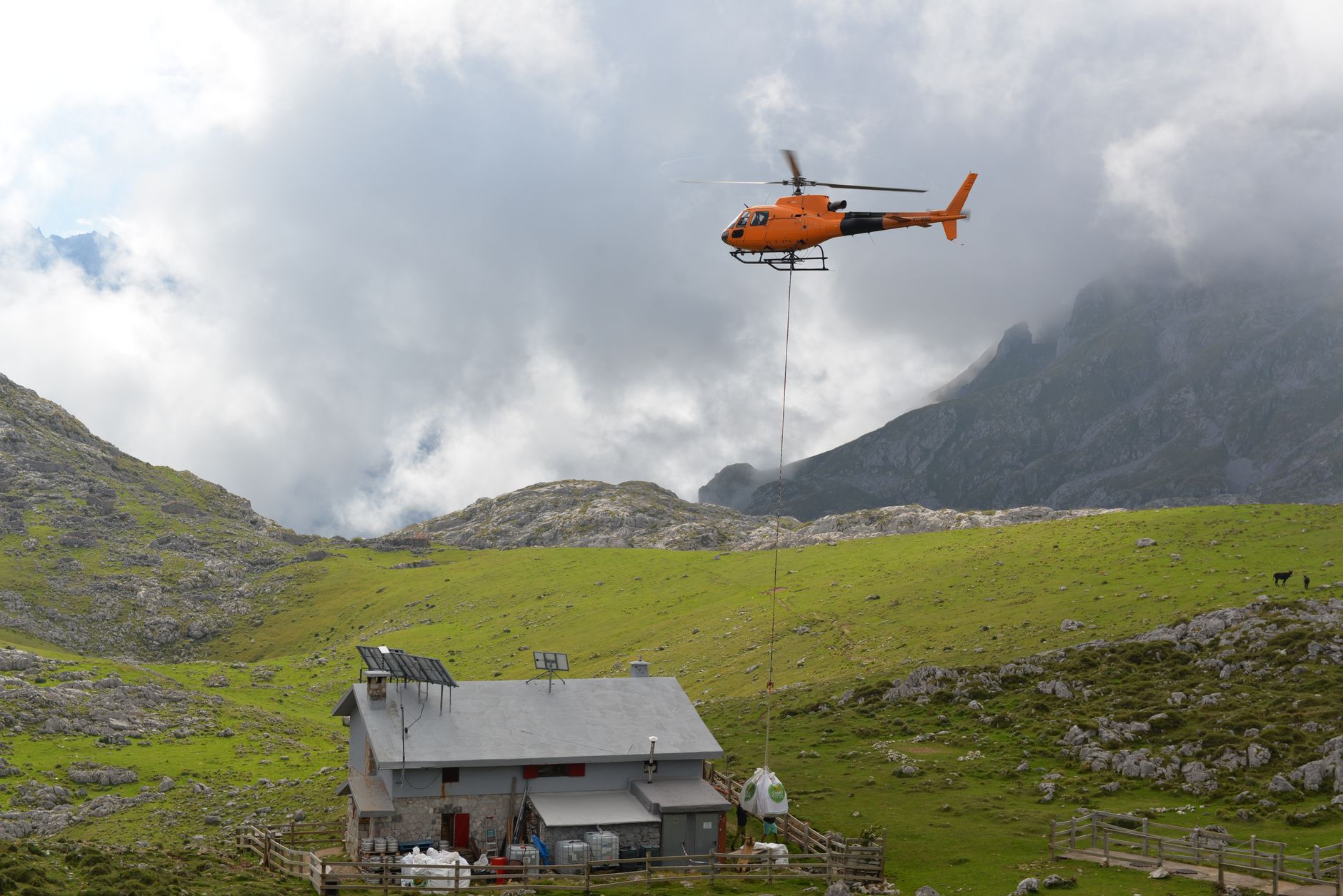 A helicopter transports goods mid-flight over a mountain hut in Picos de Europa, Onis, Spain.