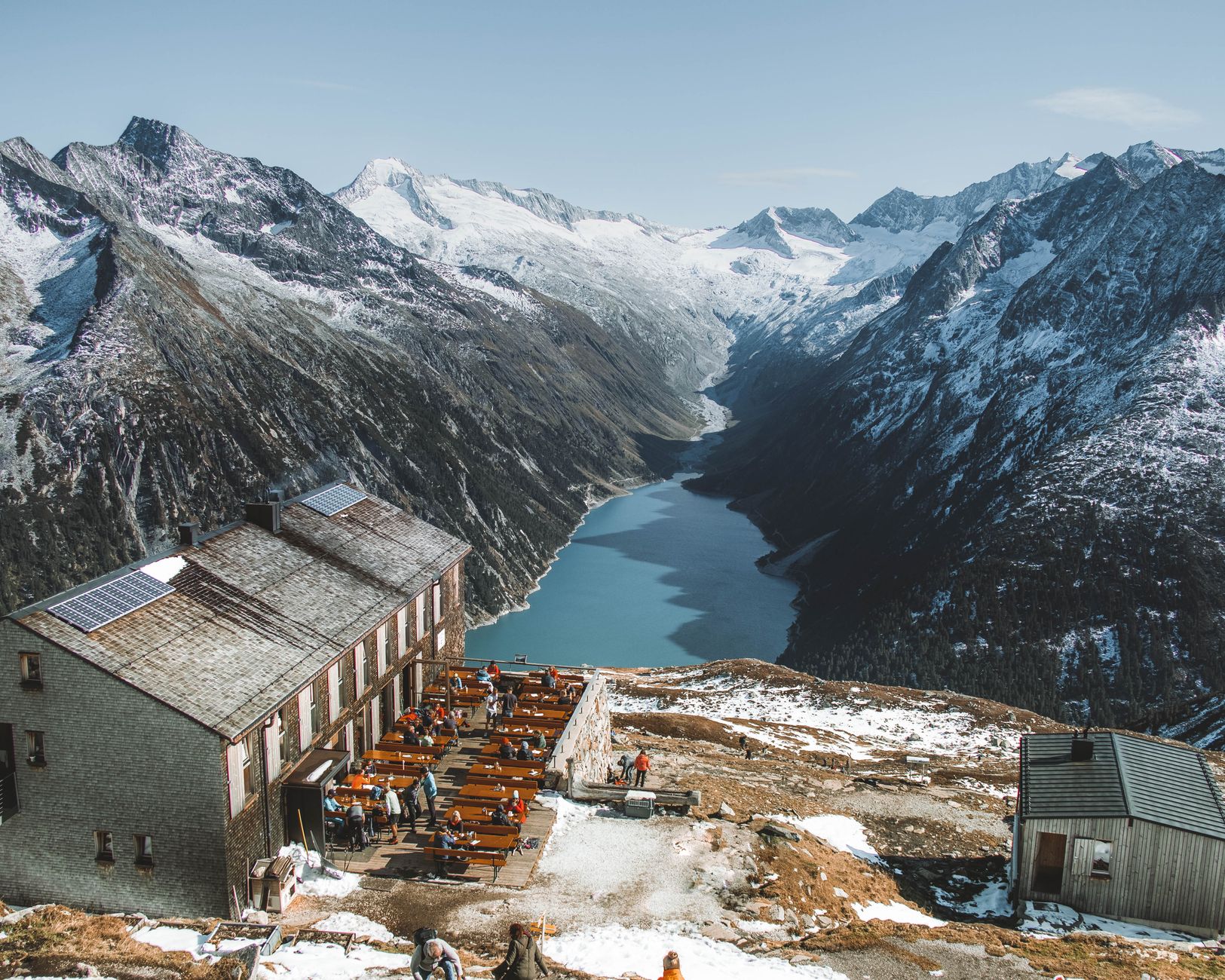 Panoramic view from the Olpererhütte overlooking a scenic alpine lake, surrounded by snow-covered peaks.
