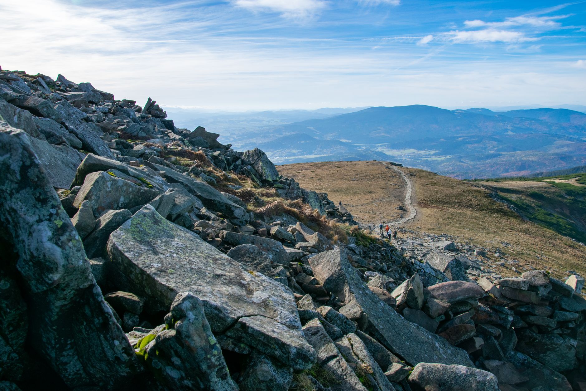 Hikers on a rocky mountain trail with breathtaking views of distant valleys and peaks.