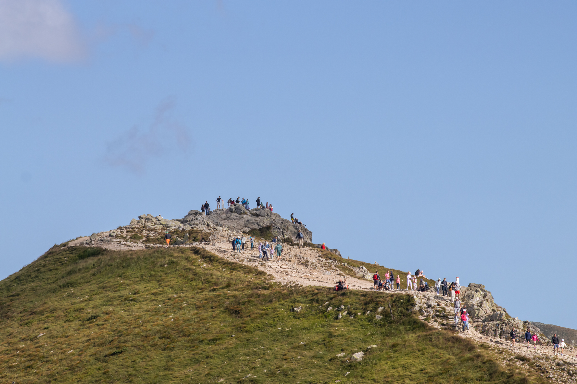 Tourists hiking on a mountain peak in Zakopane, Poland under a clear blue sky.