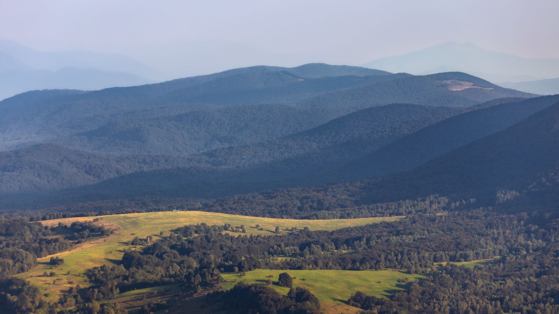 Serene landscape of the Bieszczady Mountains with lush green valleys and forested hills under a clear sky.