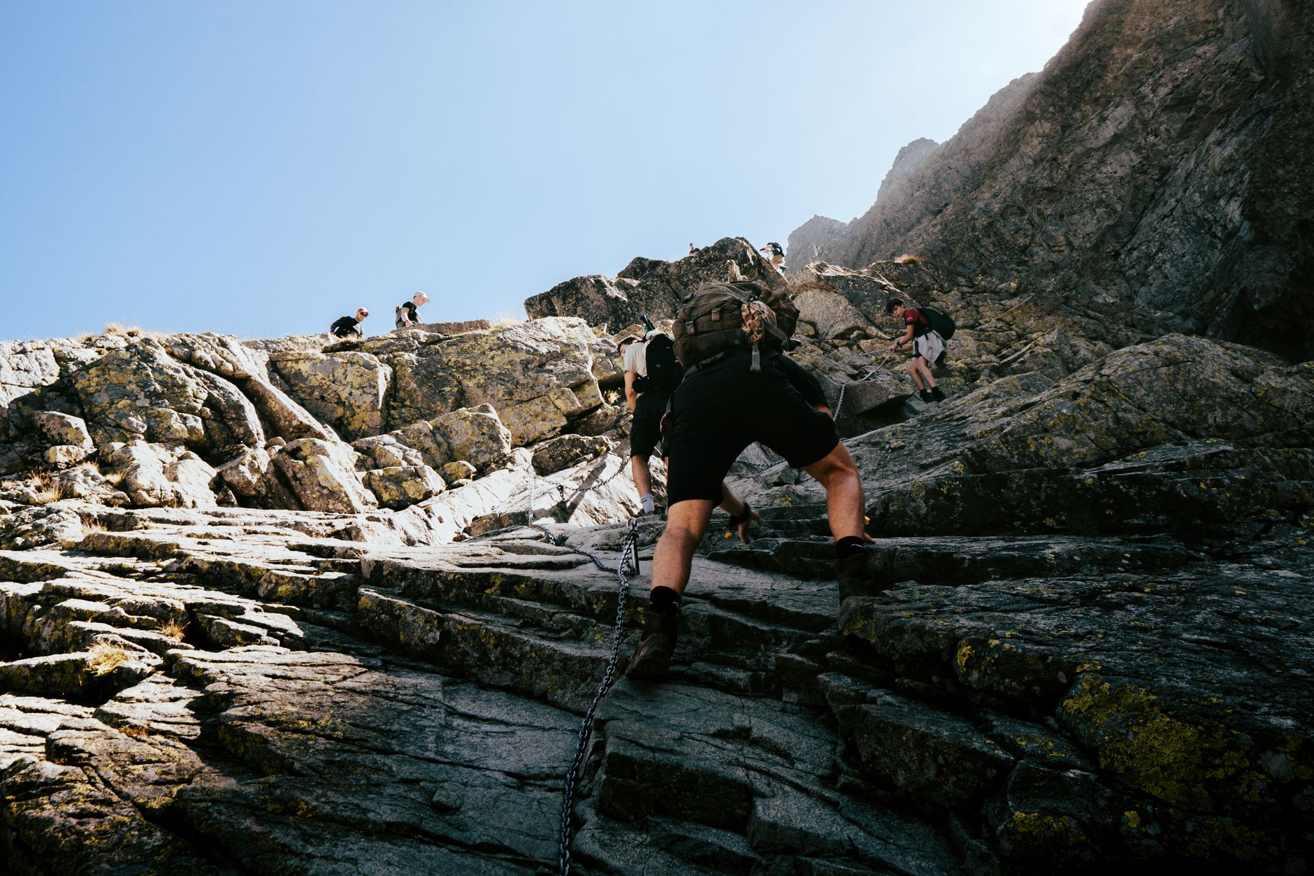 Adventurers climbing a steep, rocky path in the Tatra Mountains under a clear blue sky.