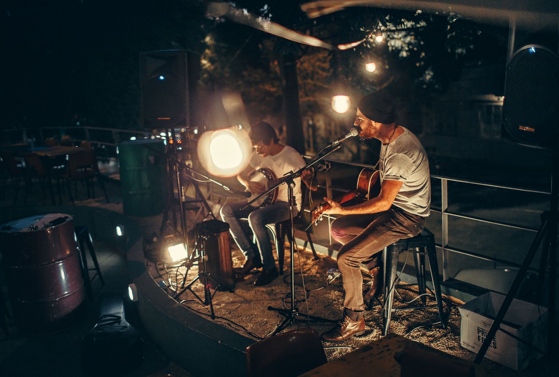 Two musicians performing acoustic music outdoors at night, illuminated by soft ambient lighting.