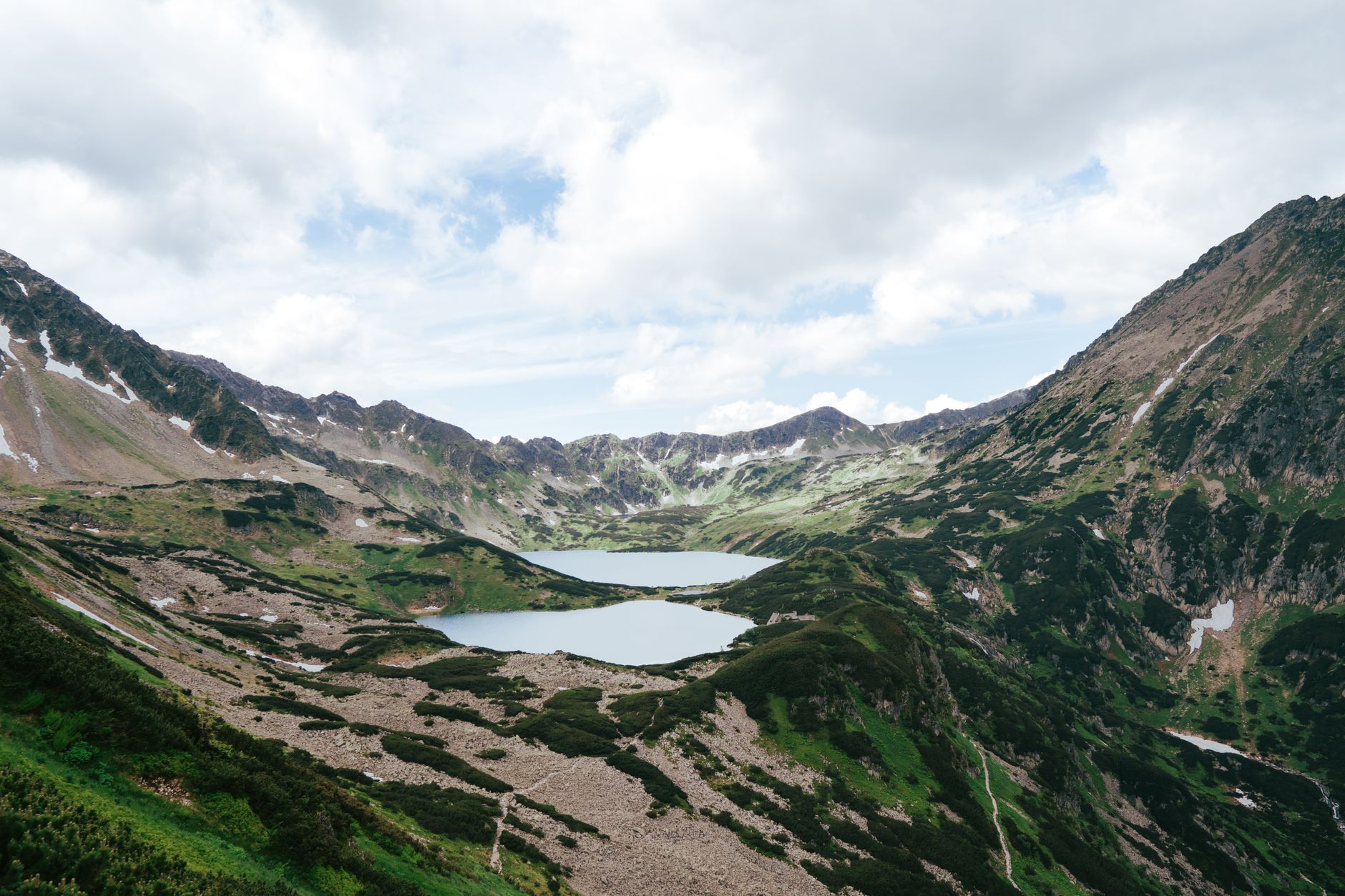 Breathtaking landscape of twin lakes surrounded by Tatra mountains under a cloudy sky.