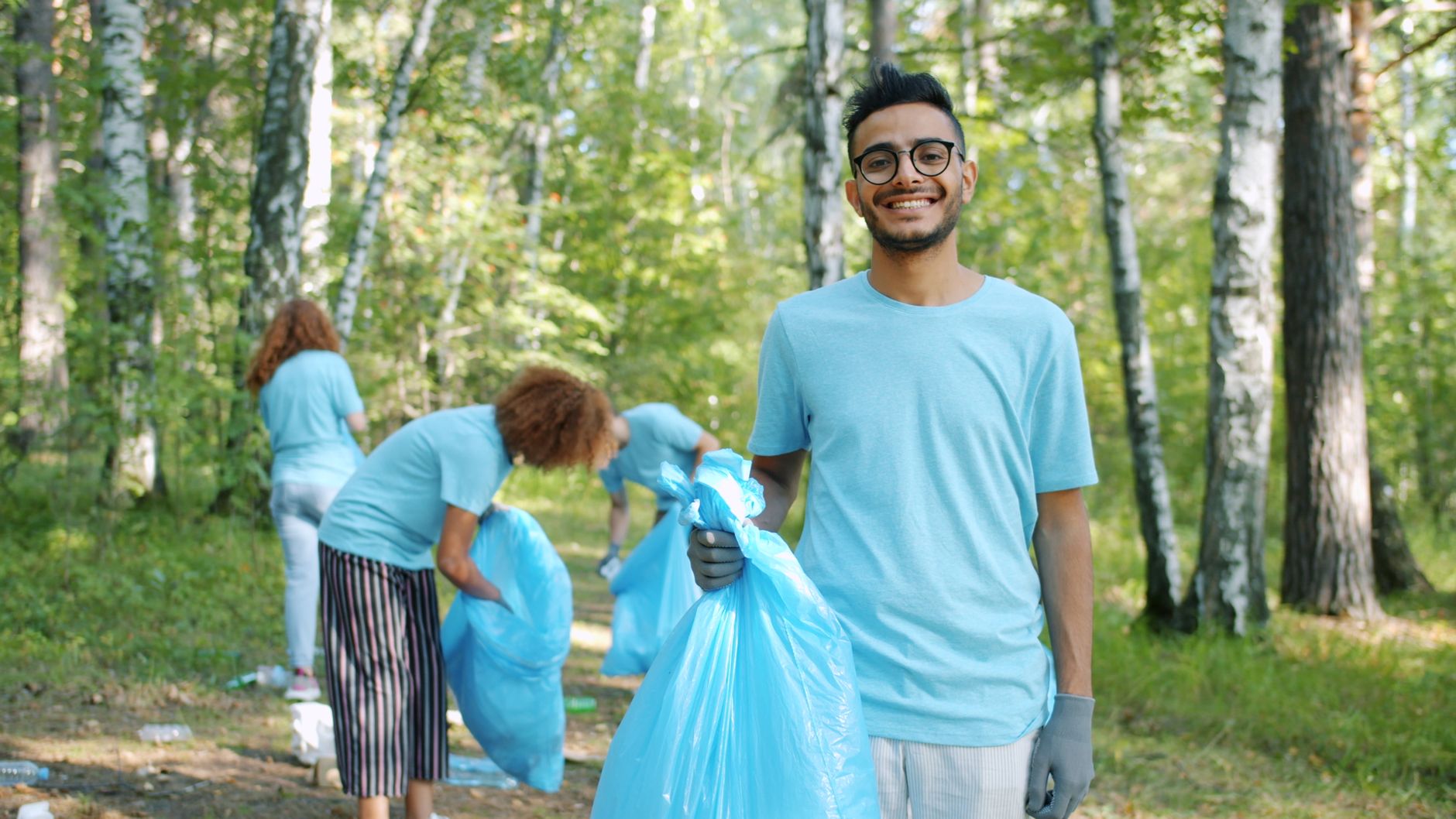 Smiling volunteers collecting litter in a sunny forest during summer.