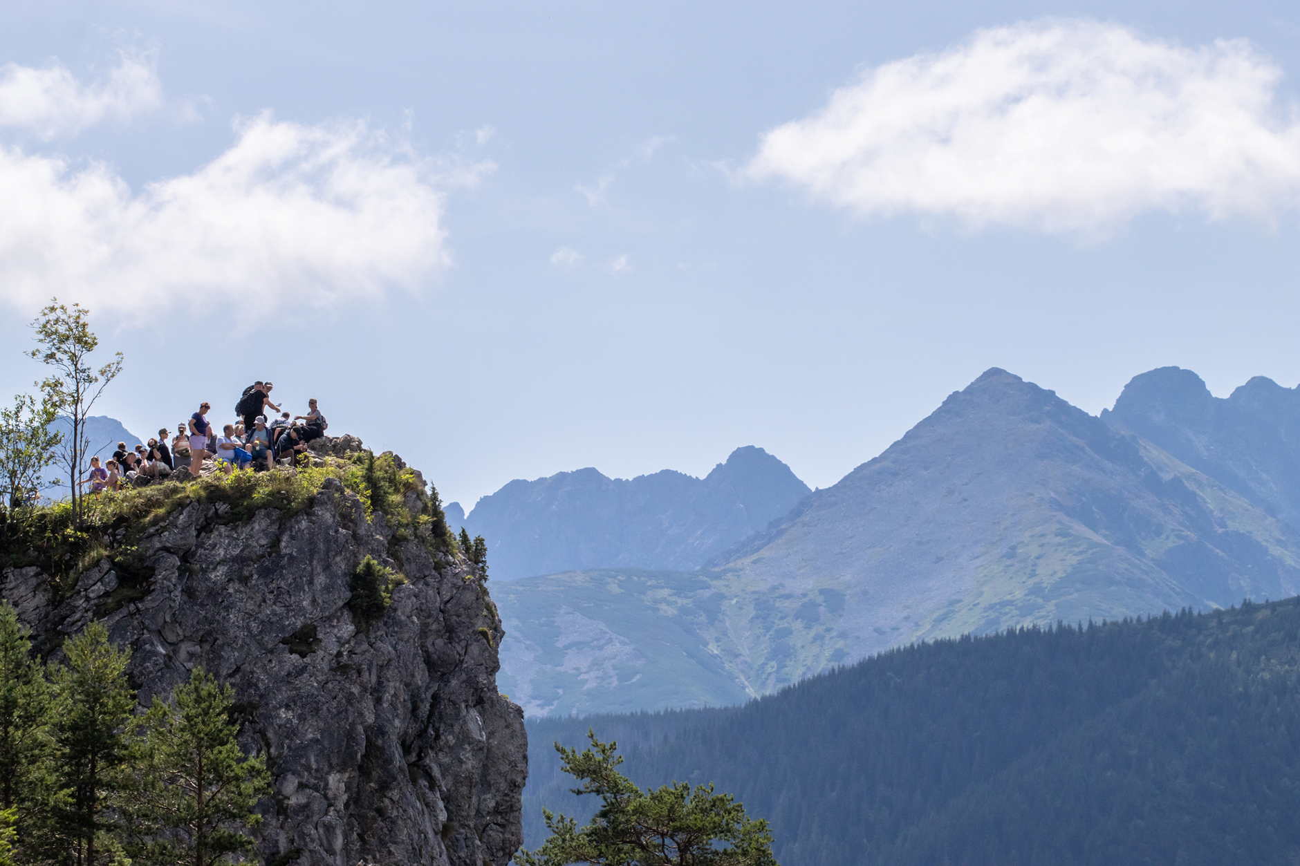 Group of hikers enjoy the view from a rocky cliff in Zakopane, Poland under a clear blue sky.