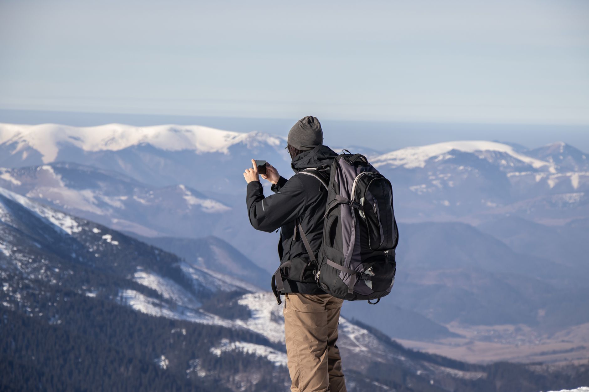 A person capturing the stunning view of snowy mountains with a smartphone.