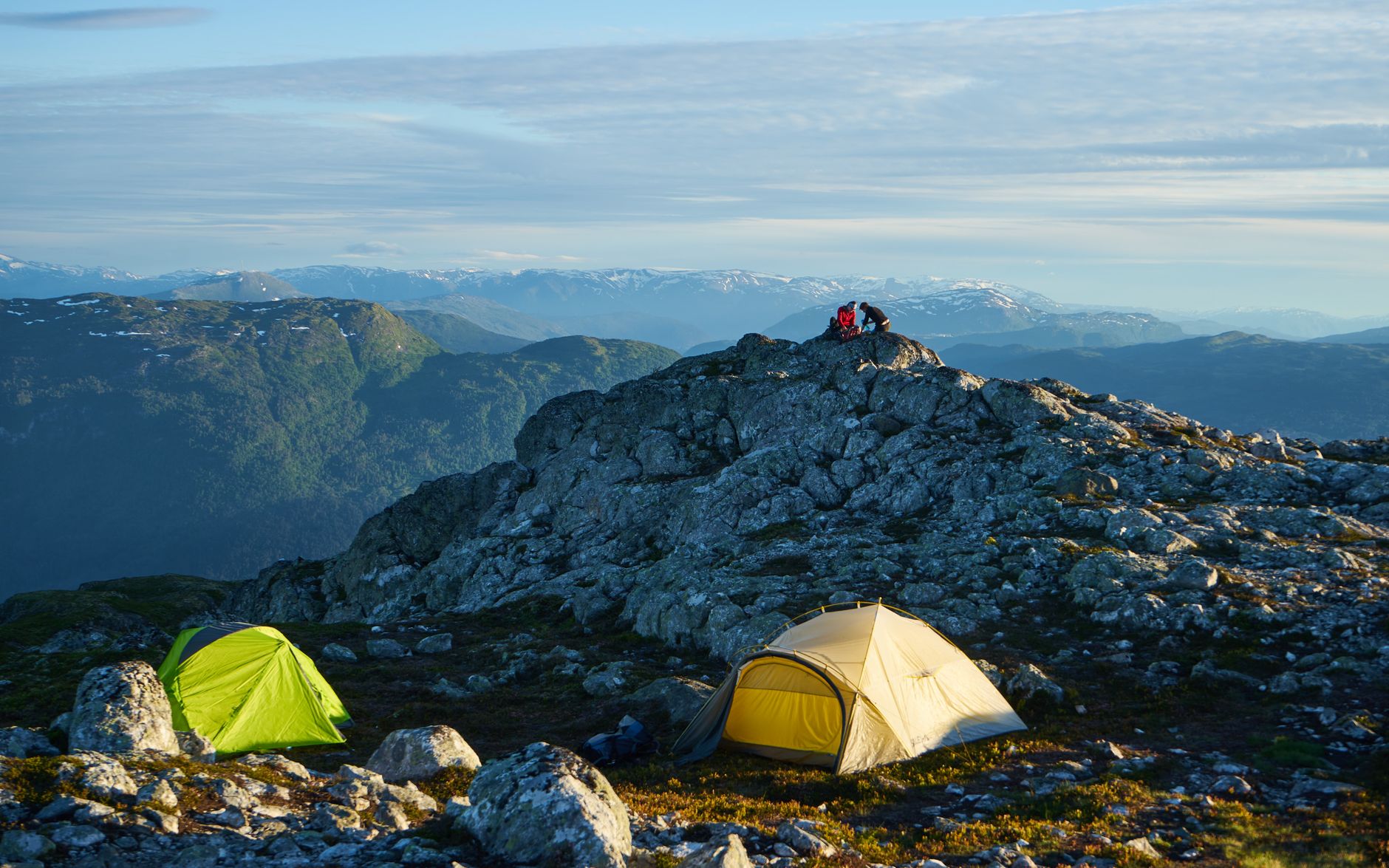 A captivating mountain camping scene with tents and rocky terrain under a clear sky.