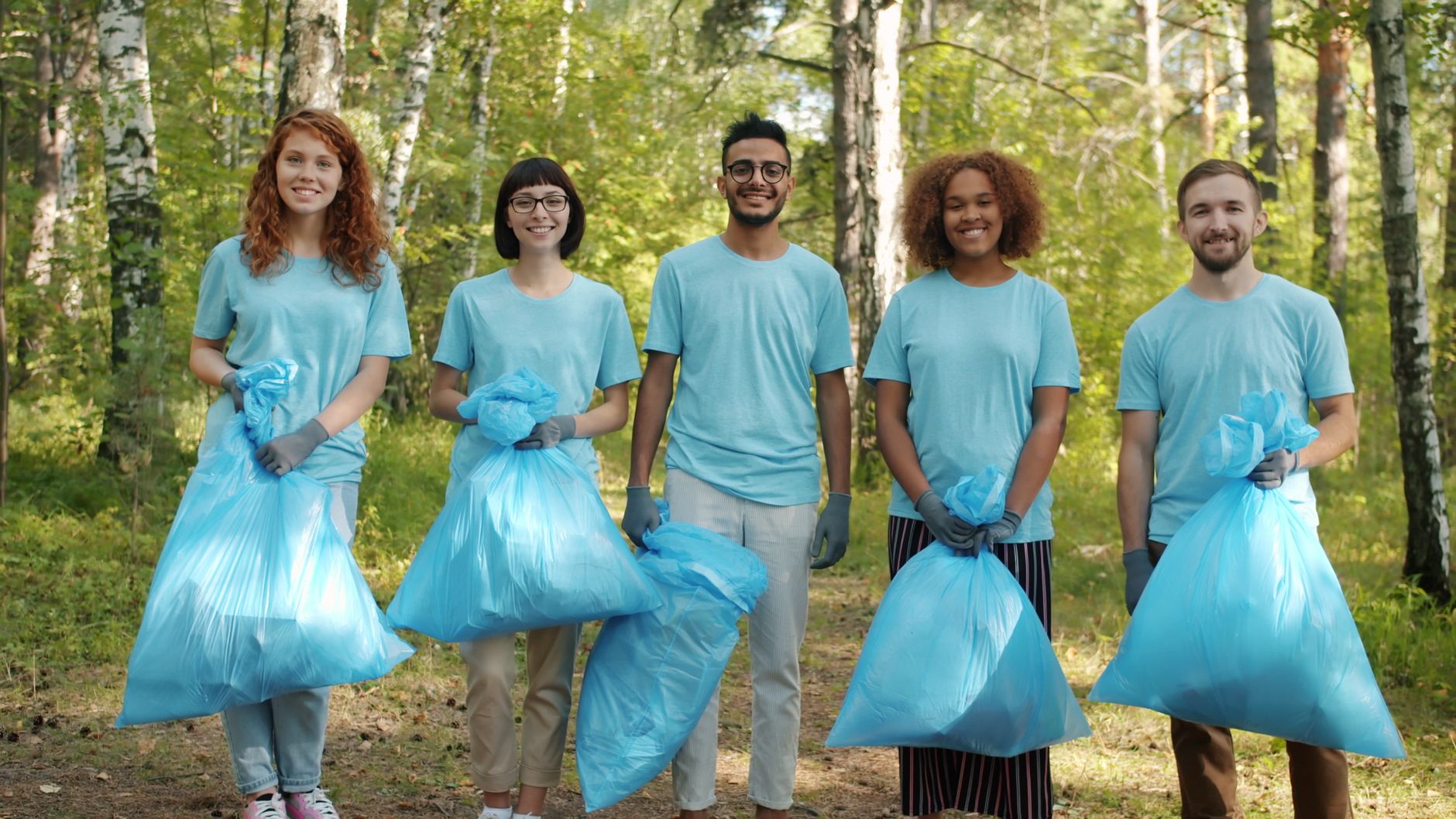 A diverse group of young adults volunteering to clean up a forest area.
