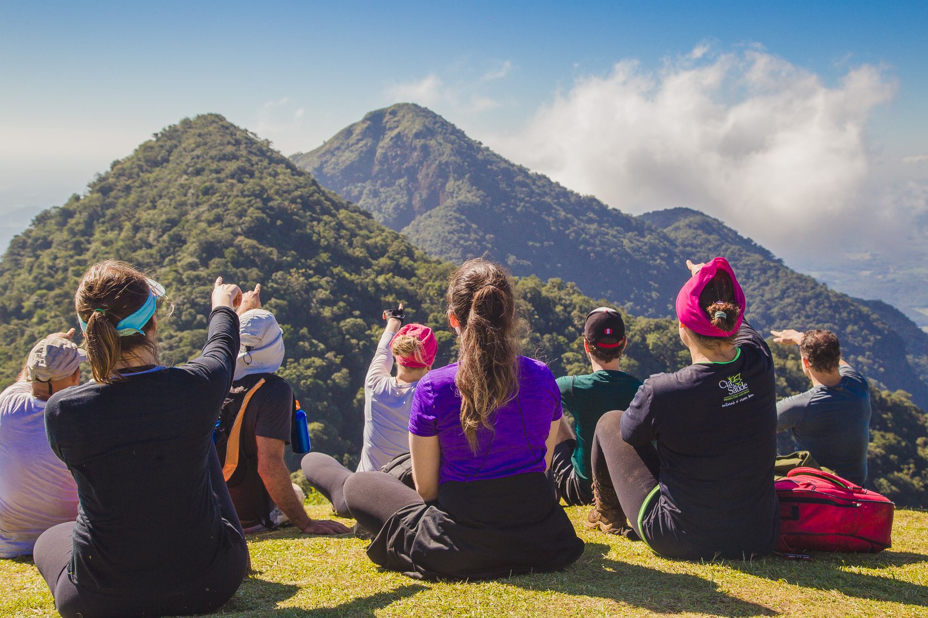 A diverse group of hikers enjoying a scenic mountain view while sitting on grass during the day.