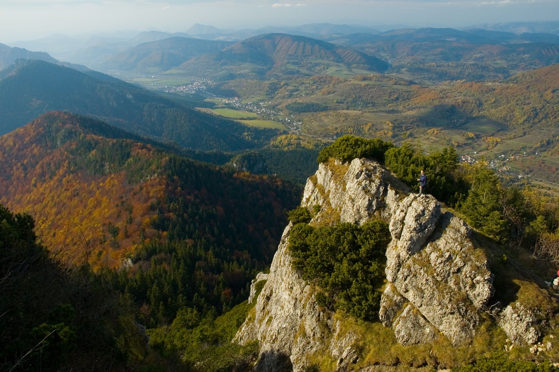 A breathtaking aerial view of a rocky mountain landscape with autumn colors and a solitary hiker.