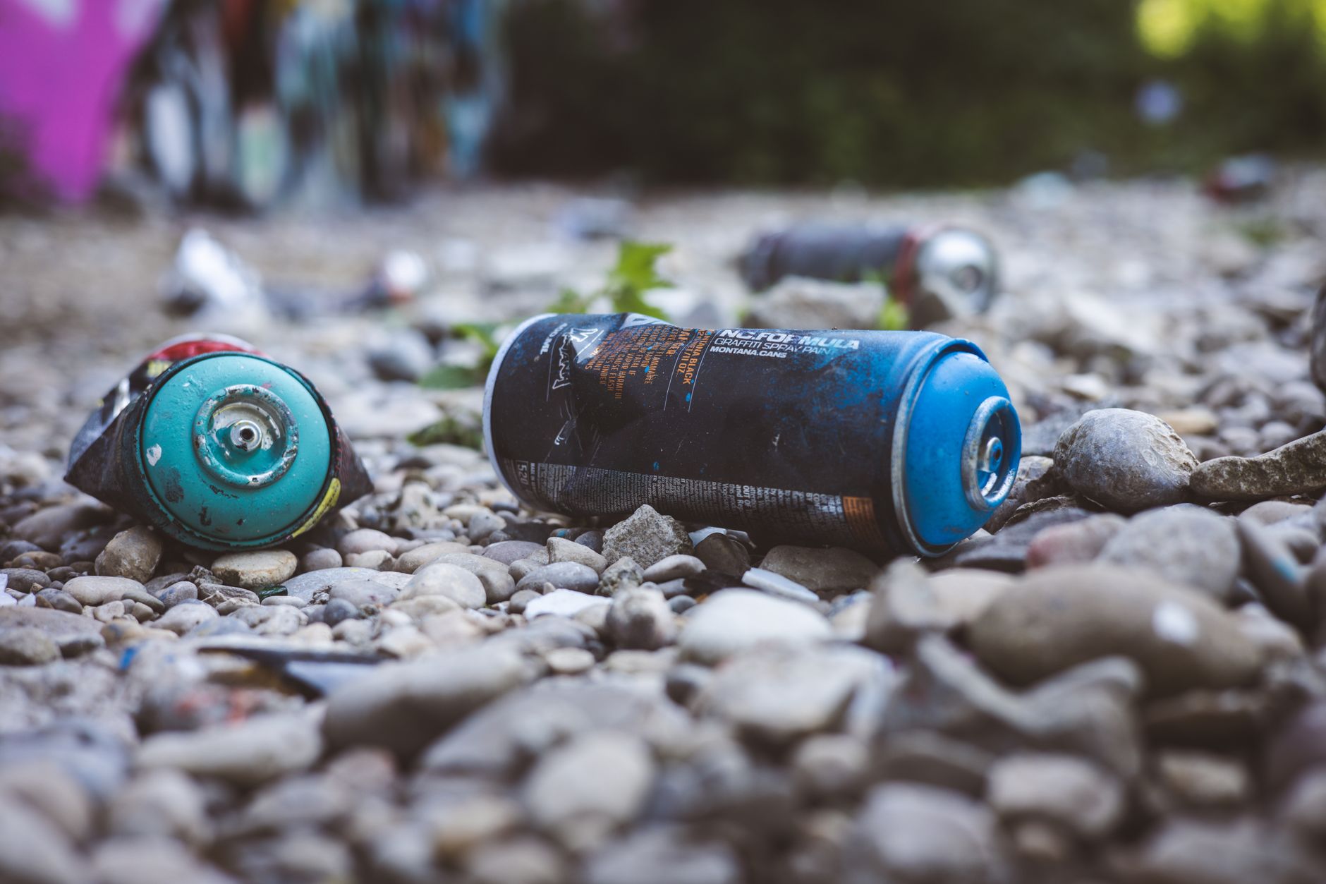 Close-up photo of discarded spray cans on rocky ground in outdoor setting, highlighting environmental waste.