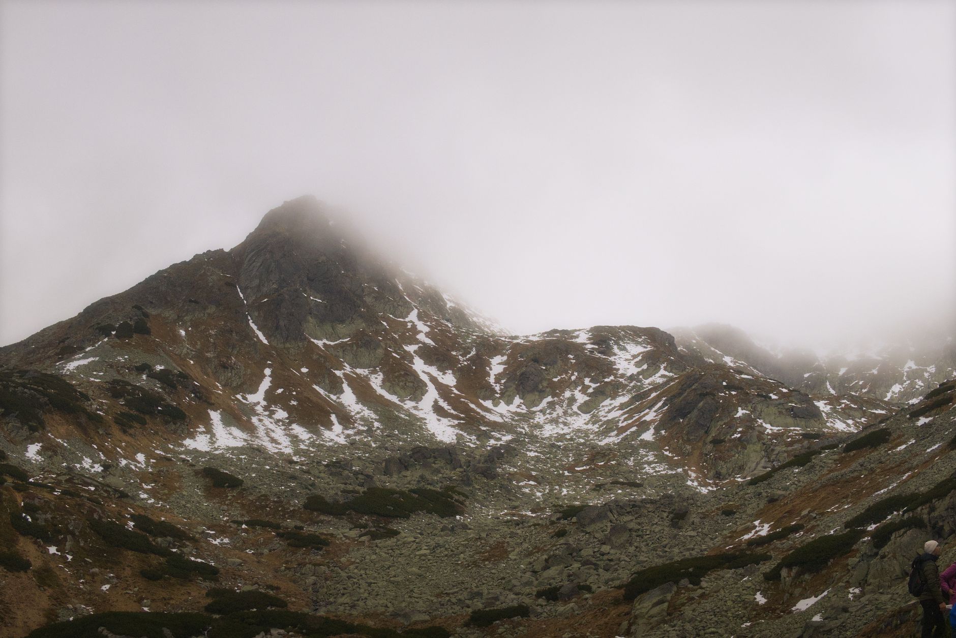 A captivating view of the misty peaks of Slovakia's High Tatras mountains during fall, with scattered snow and rugged terrain.