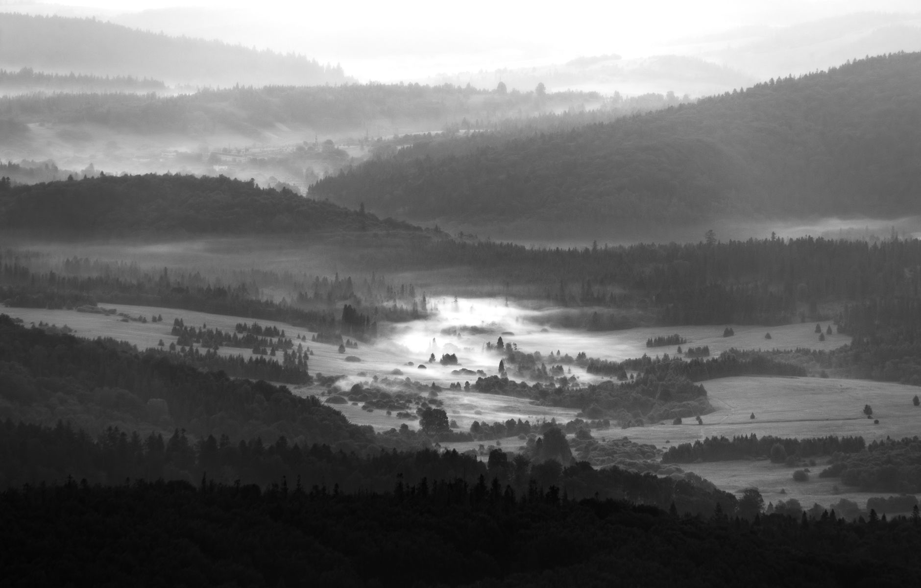 A breathtaking view of misty valleys and forested hills in the Bieszczady Mountains at sunrise.