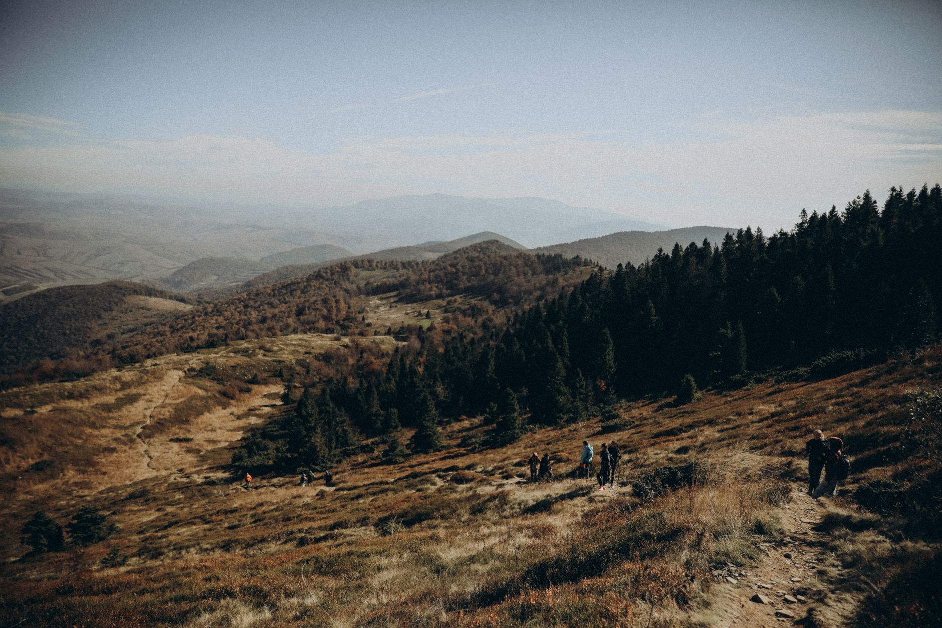 Hikers enjoying a scenic mountain trail in autumn, surrounded by forest and rolling hills.