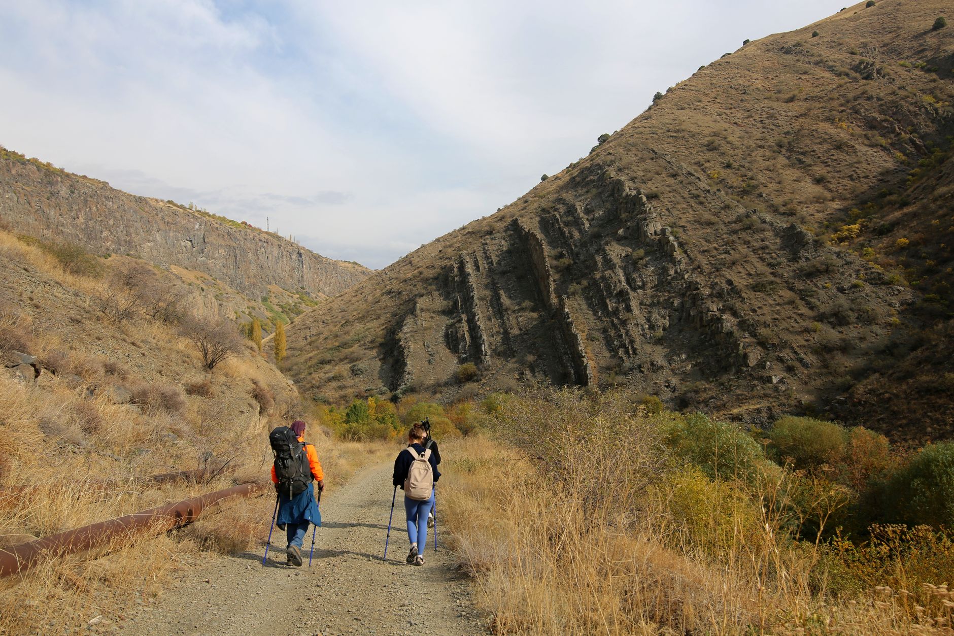 Two hikers traverse a scenic mountain trail amidst rocky landscapes and autumn foliage.