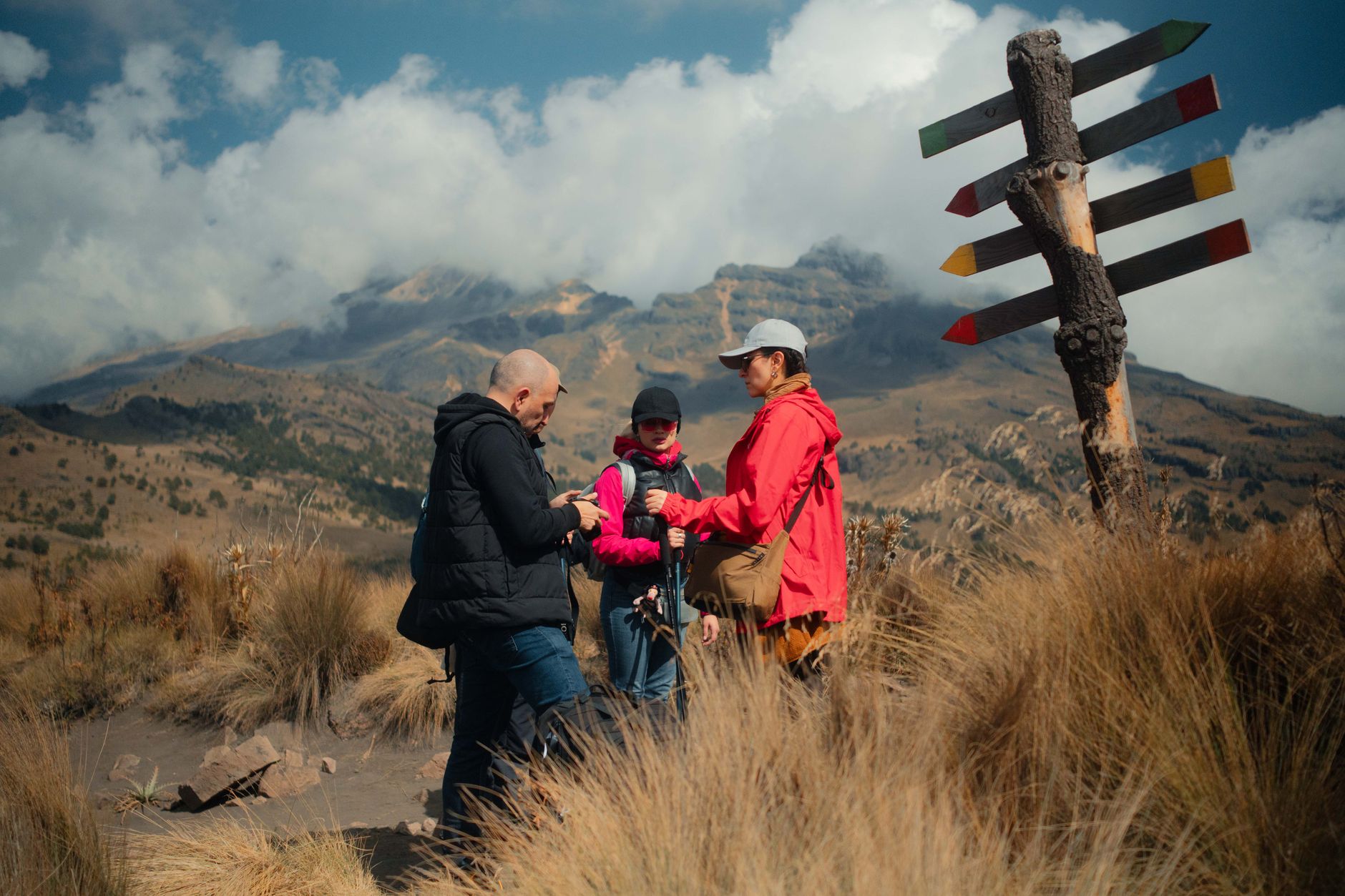 A group of hikers enjoying a scenic mountain trek with a signpost and clouds above.