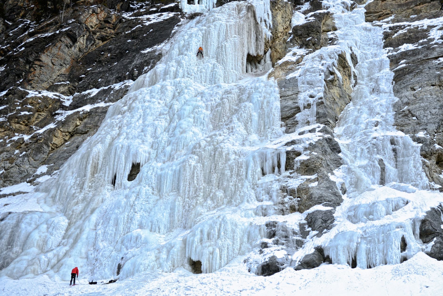 Adventurous ice climbers challenge a towering frozen waterfall on a rugged mountainside in winter.
