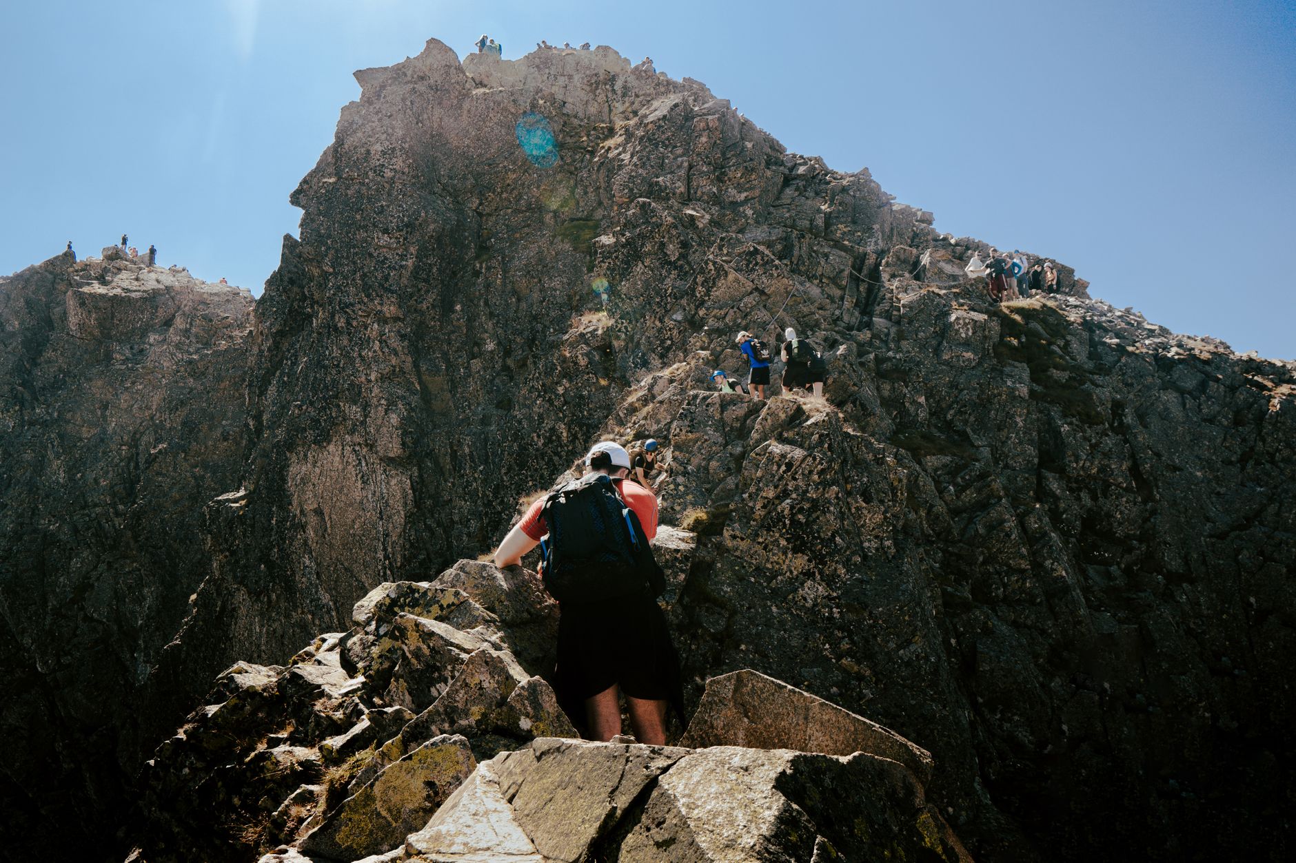 Adventurous hikers climbing rocky ridge in Tatra Mountains under clear blue sky.