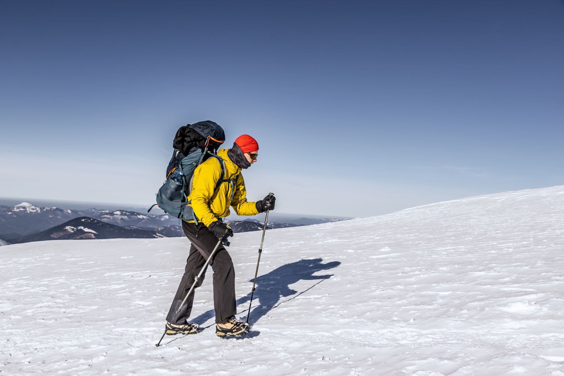 A hiker in bright winter gear ascends a snowy mountain during the day, showcasing outdoor adventure.