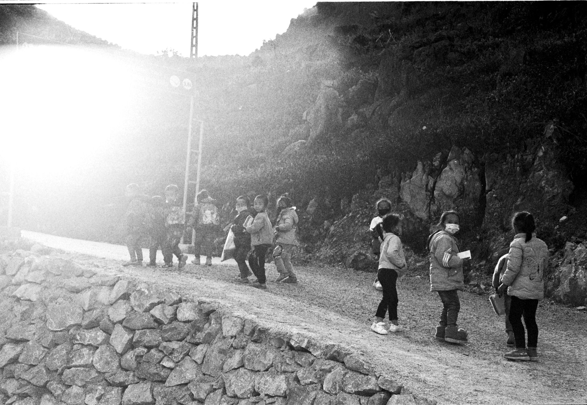 Children walking on a mountain path amidst sunlight, showcasing adventure and exploration.