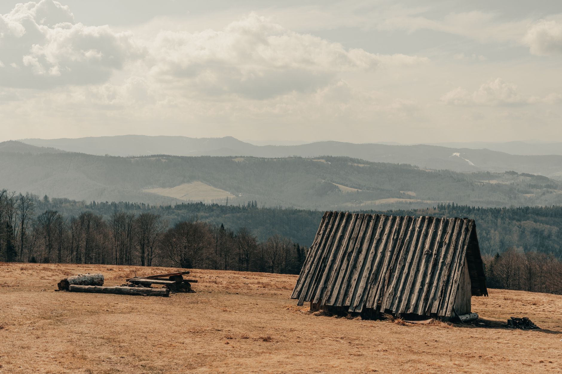 A rustic wooden shelter sits amidst the serene mountain landscape of Brenna, Poland.