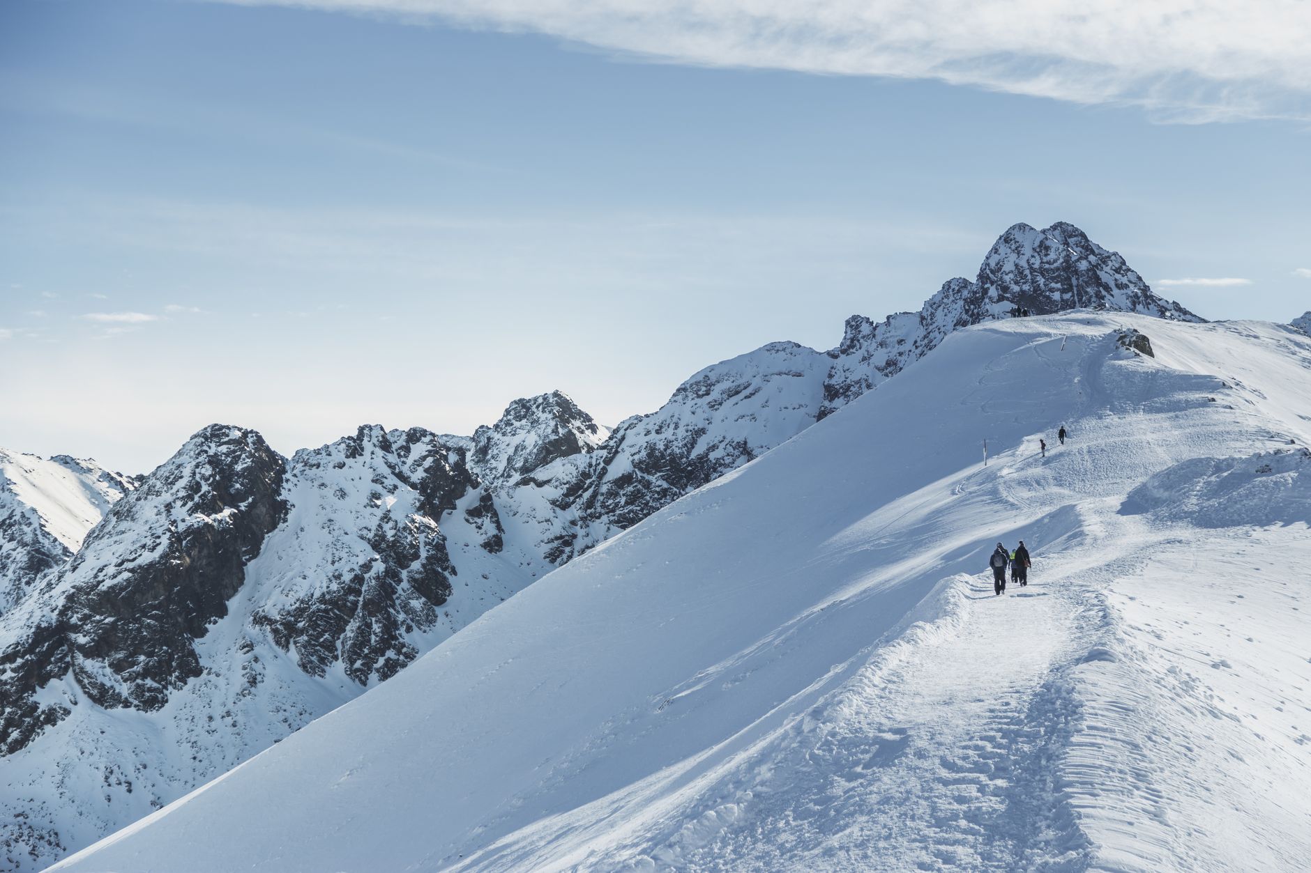 Hikers traverse a stunning snowy mountain ridge under a clear blue sky.