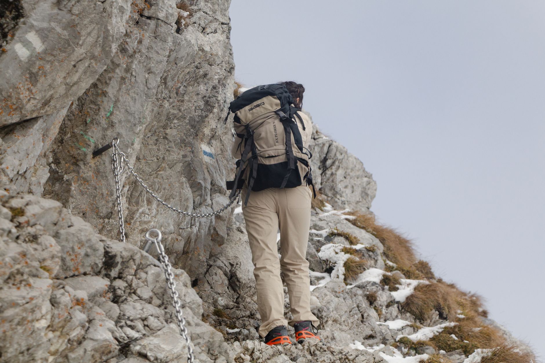 Hiker in beige outfit climbing rocky mountain with chains for support in Poland.