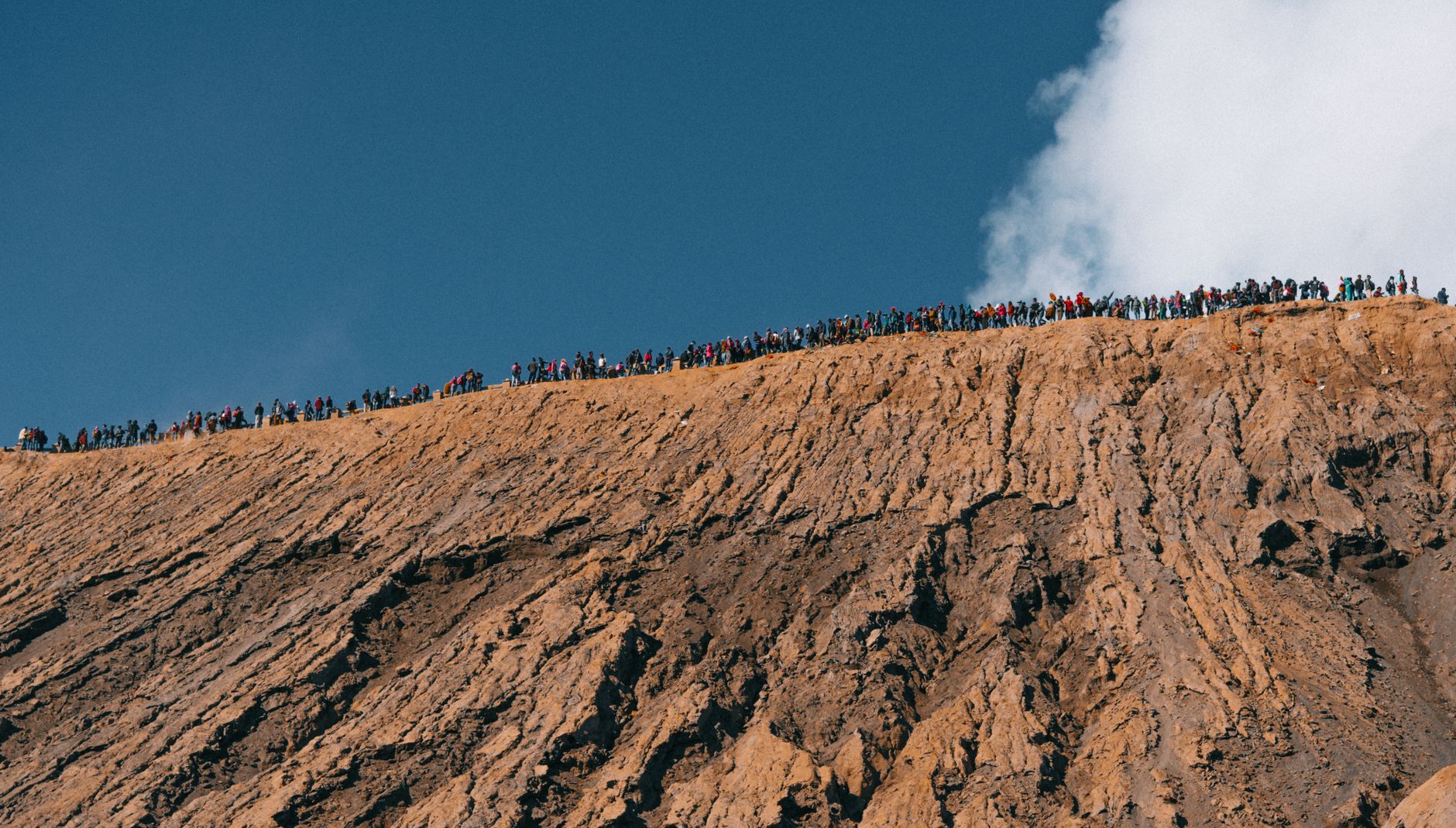 A large group of people hiking along a rugged mountain ridge under a clear blue sky.