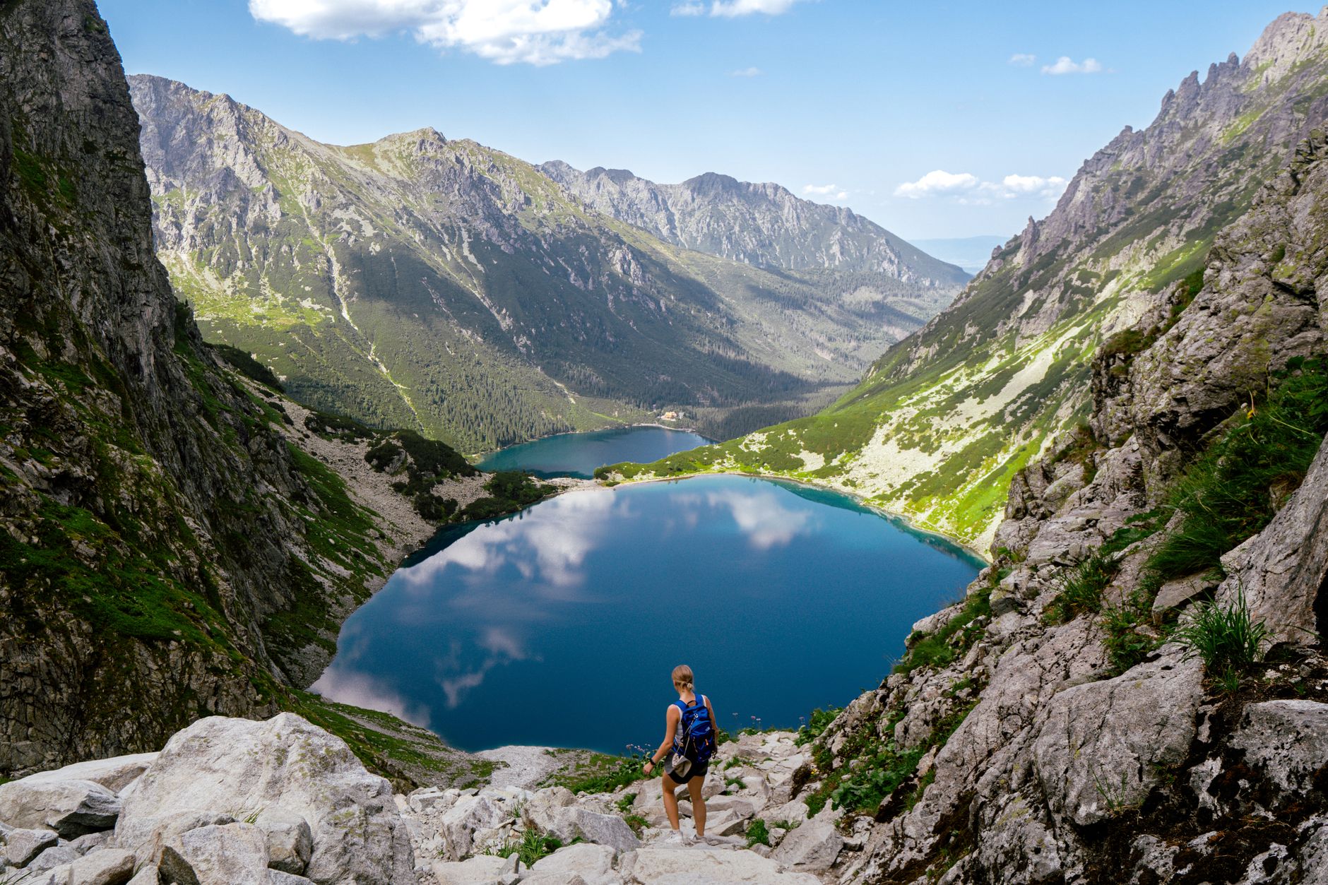 A hiker enjoys a breathtaking view of a blue alpine lake surrounded by Tatra Mountains in Zakopane, Poland.